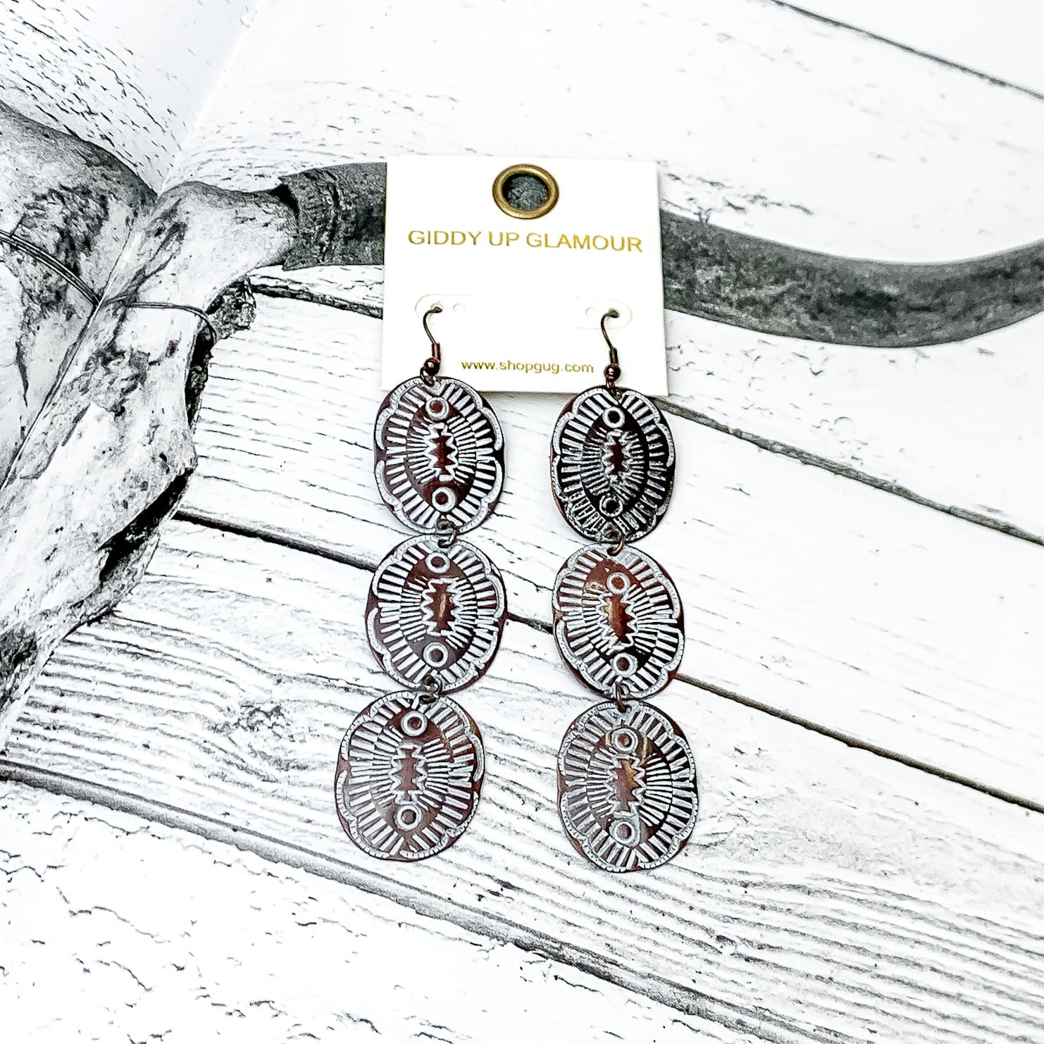 Three Tier Copper Tone Oval Earrings With White Designs. Pictured on a western page of a book with wood and a longhorn.