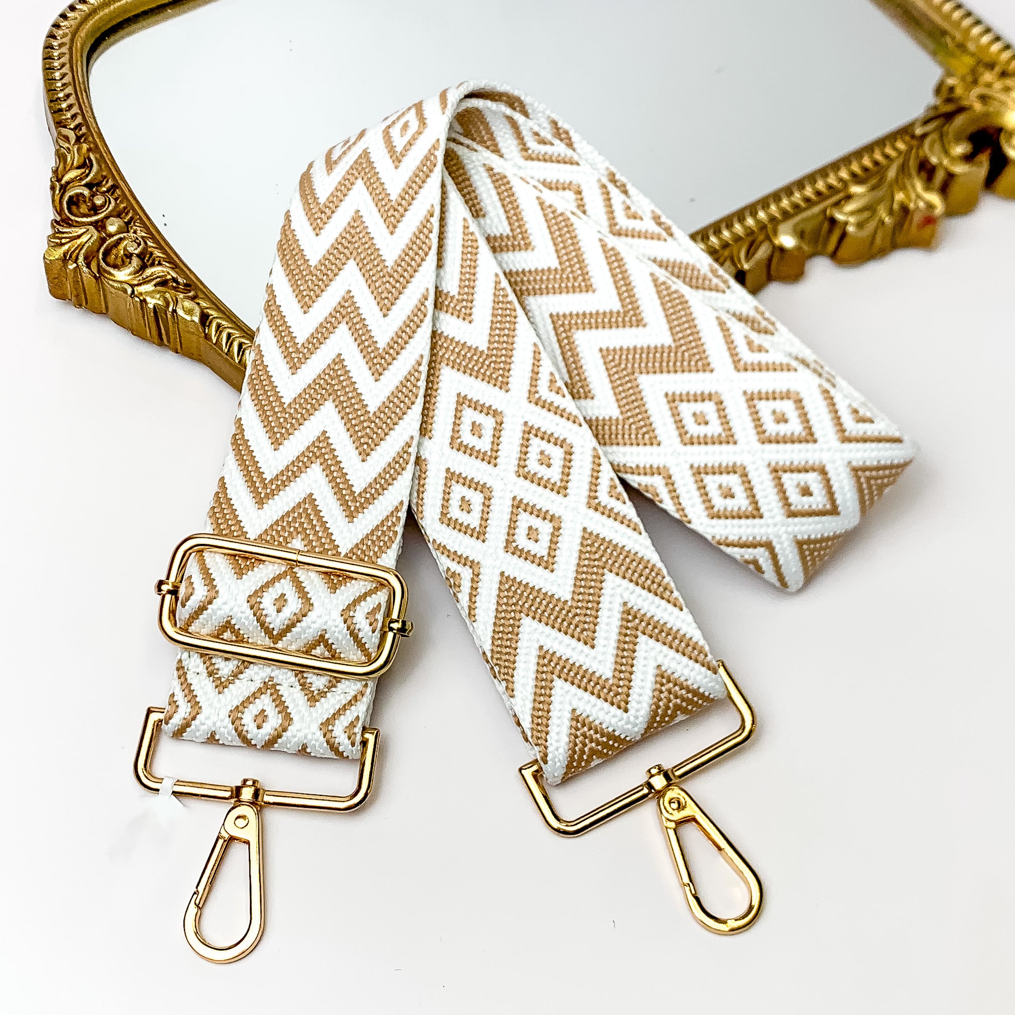 Beaige canvas purse strap with white and beige chevron and diamond design. This purse strap includes gold accents. This purse strap is pictured partially on a gold mirror on a white background.