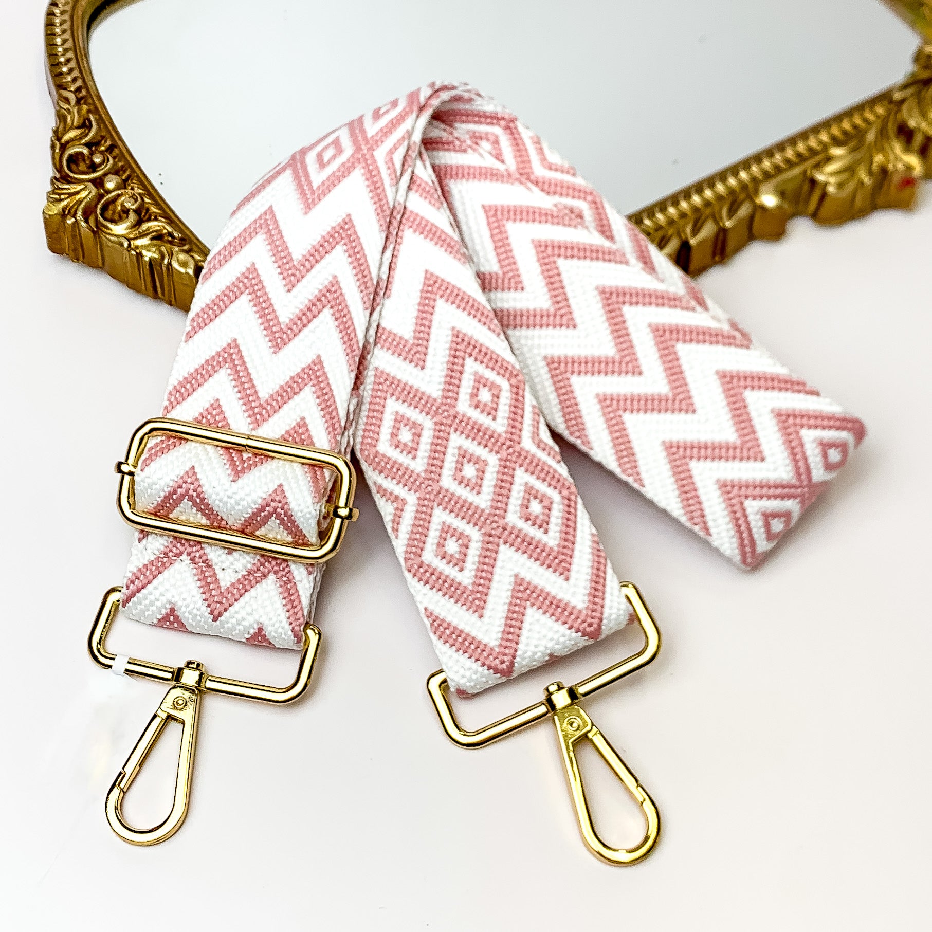 Beaige canvas purse strap with white and baby pink chevron and diamond design. This purse strap includes gold accents. This purse strap is pictured partially on a gold mirror on a white background.