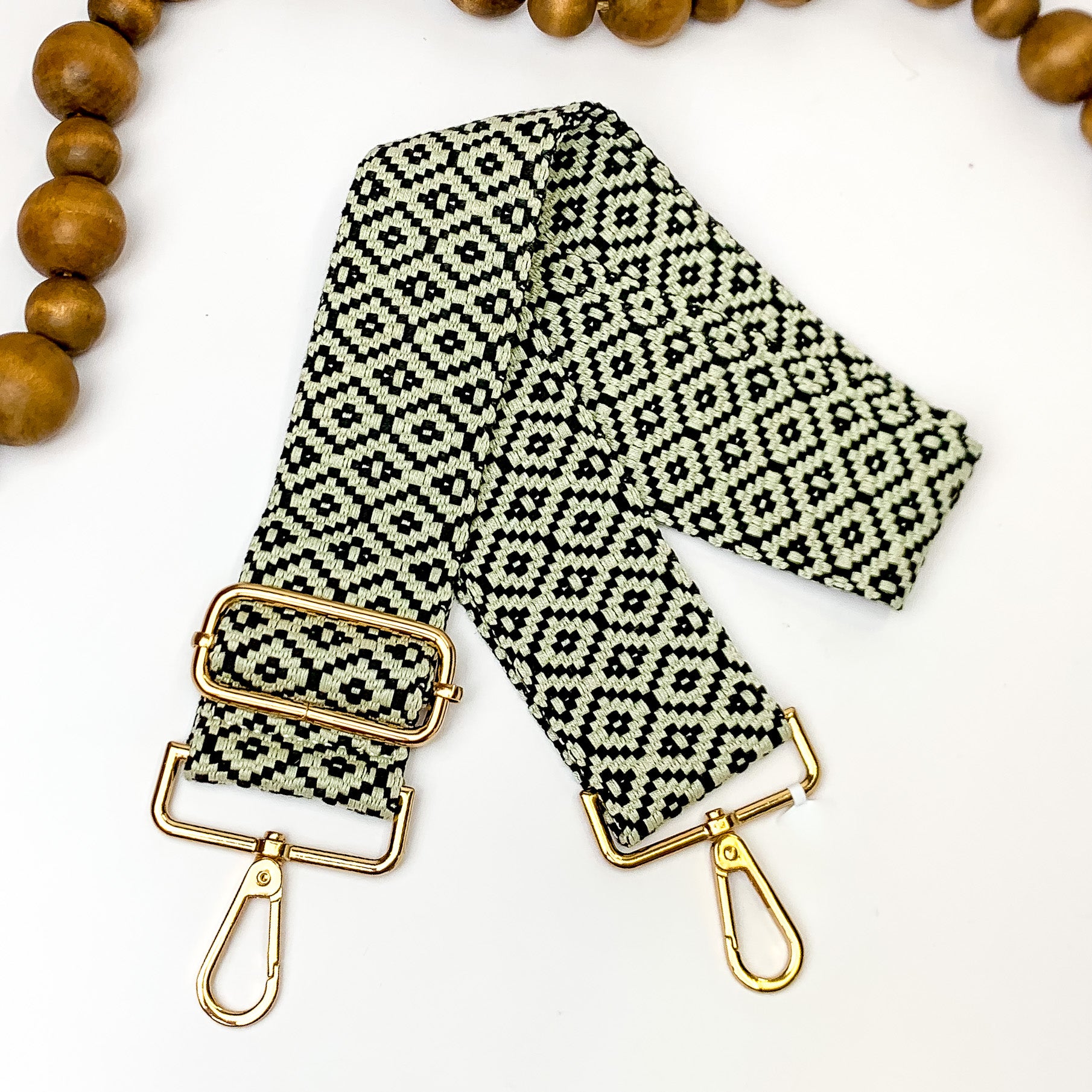 Beaige canvas purse strap with black diamond design. This purse strap includes gold accents. This purse strap is pictured on a white background with brown beads at the top.