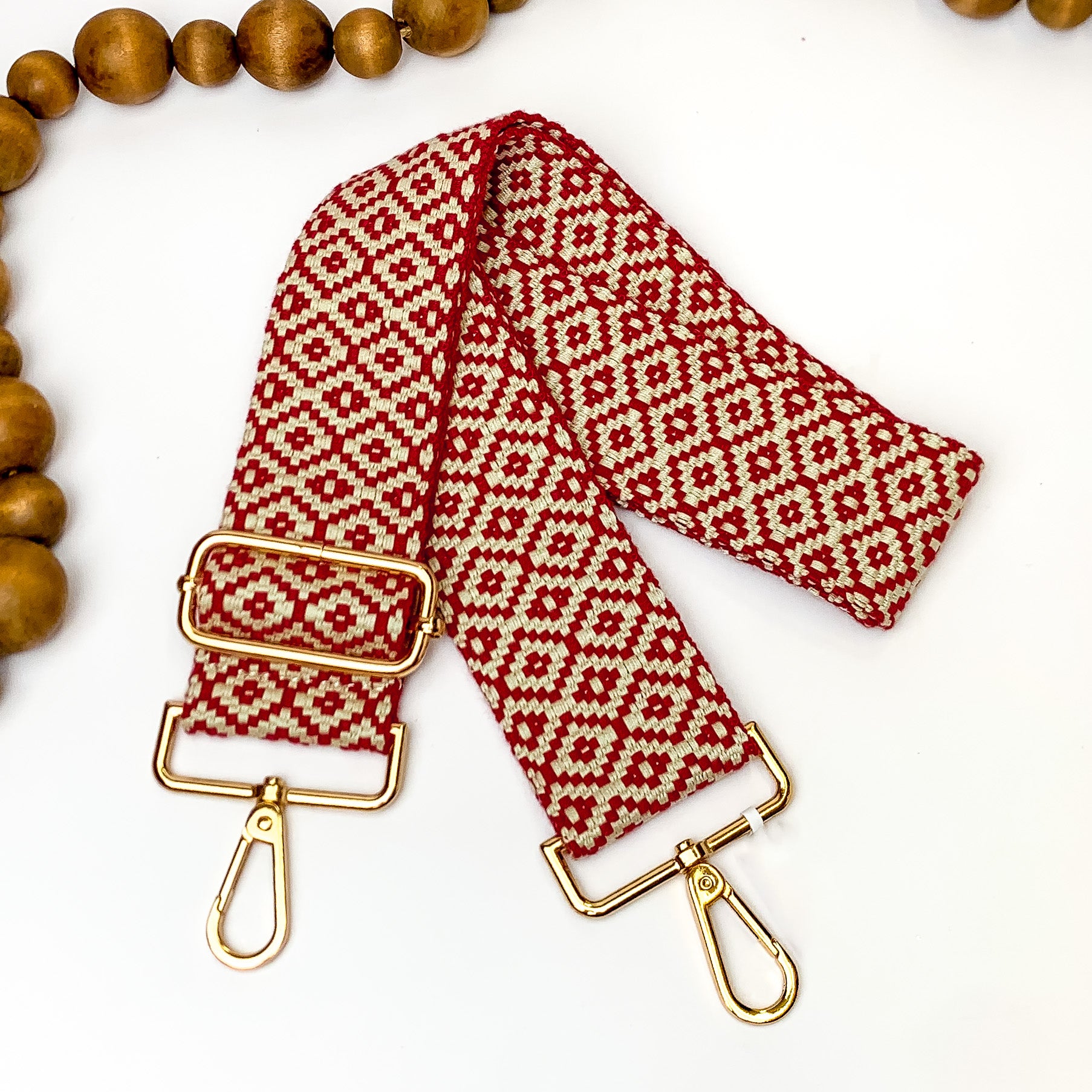 Beaige canvas purse strap with dark red diamond design. This purse strap includes gold accents. This purse strap is pictured on a white background with brown beads at the top.