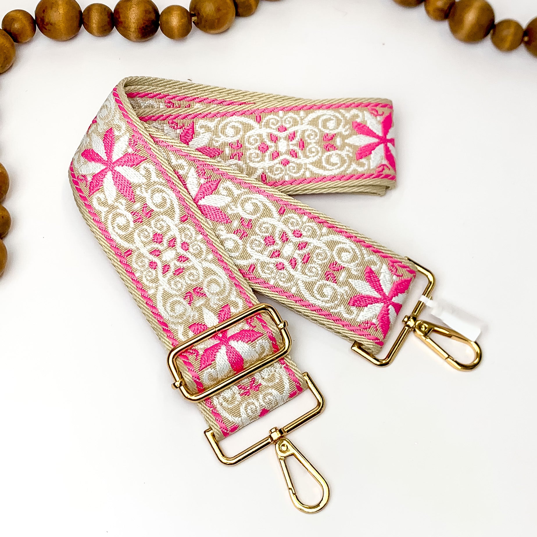 Beige canvas purse strap with white and pink embroidered design. This purse strap includes gold accents. This purse strap is pictured on a white background with wood beads at the top.
