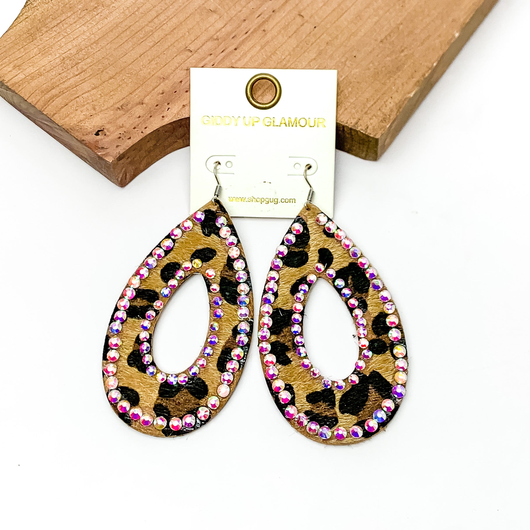 Leopard Print Open Teardrop Earring With AB Crystals. Pictured on a white background with the earrings laying against a piece of wood.