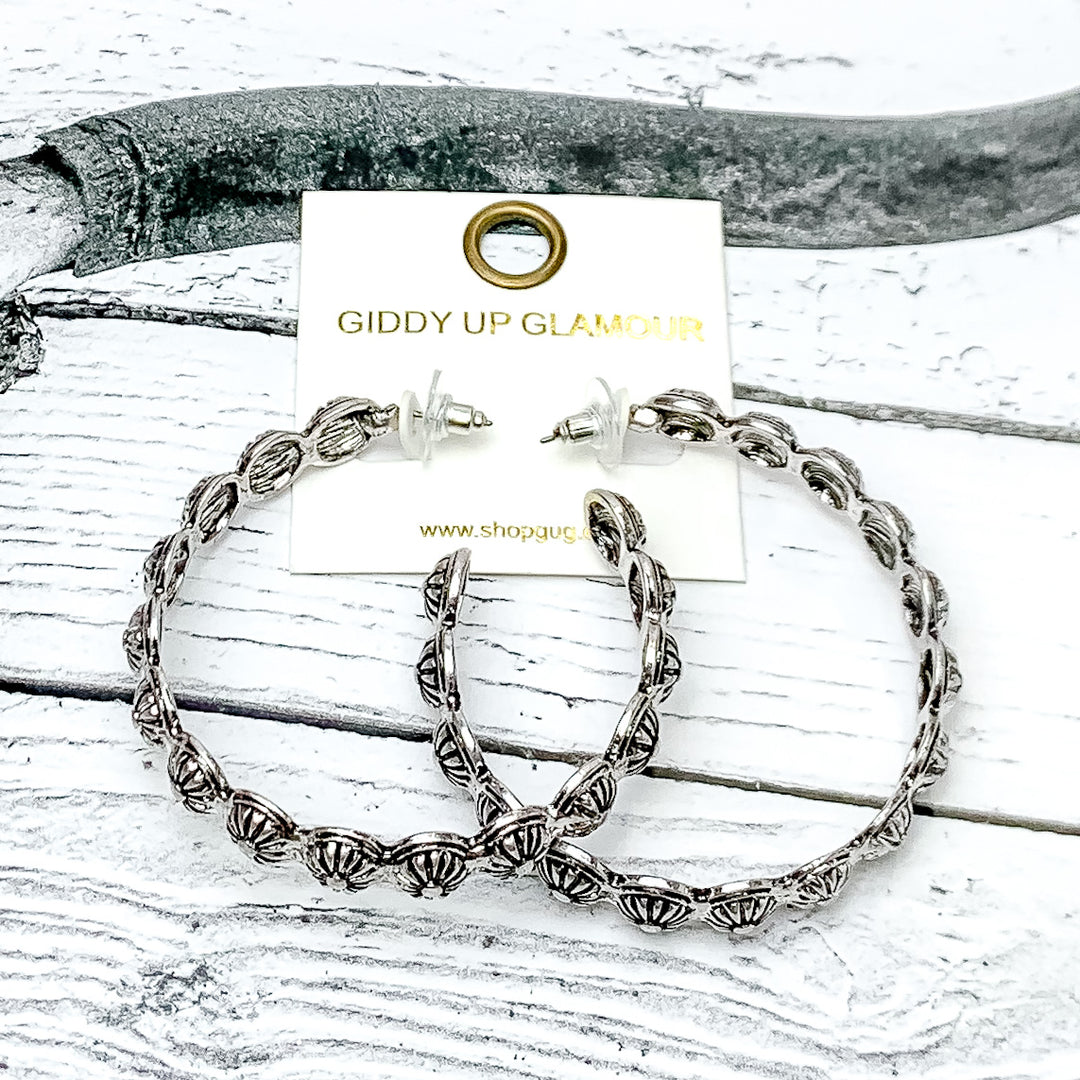 Silver Tone Large Western Earrings With Circle Designs. Pictured on a wood background with a horn through the picture. 