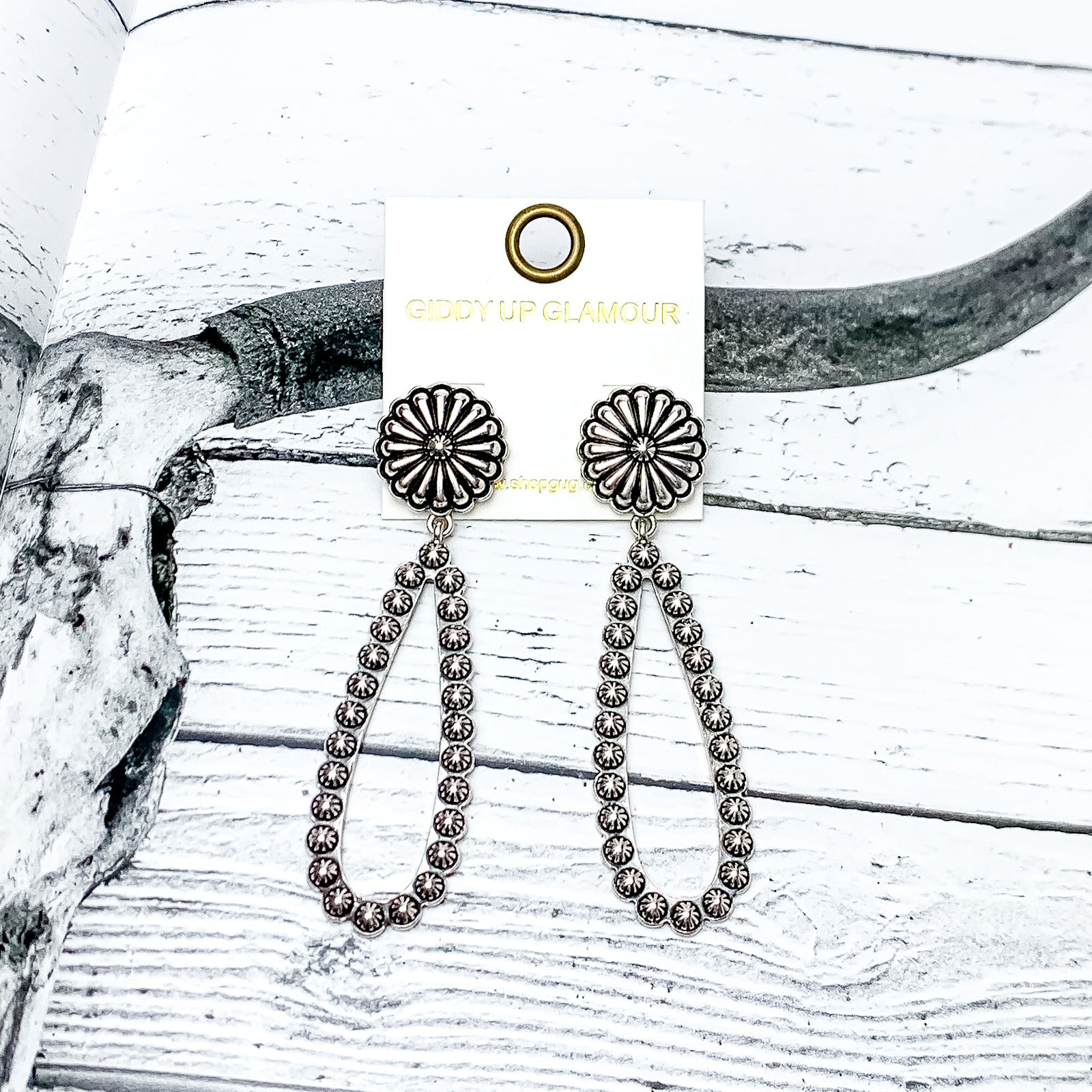 Silver Tone Open Teardrop Earrings With Flower Post. Pictured on a wood like background with a longhorn in the picture.