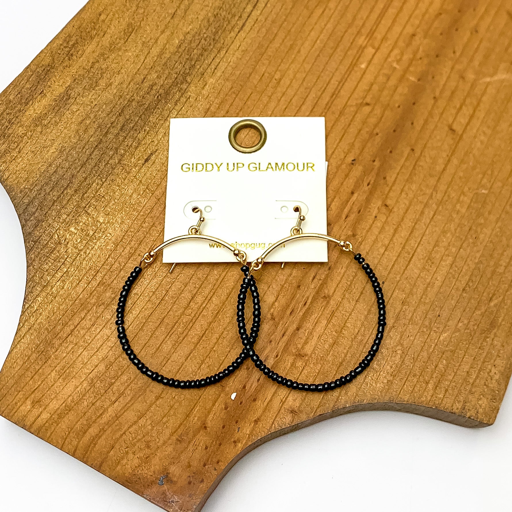 Gold Tone Hoop Earrings Beaded in Black. Pictured on a piece of wood.