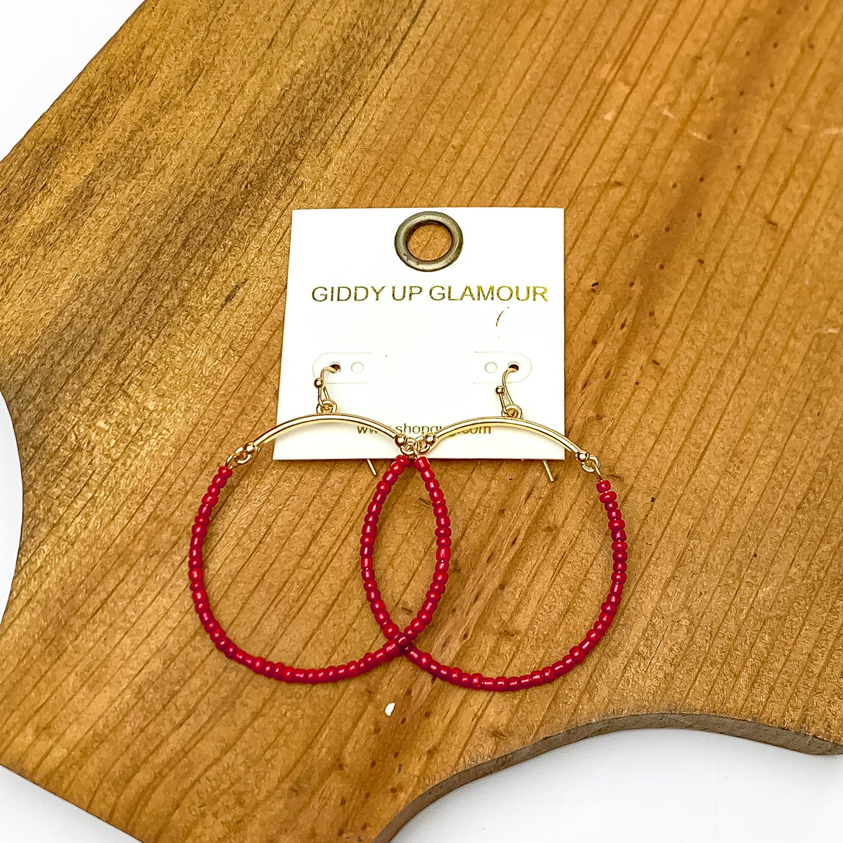 Gold Tone Hoop Earrings Beaded in Maroon. Pictured on a piece of wood.