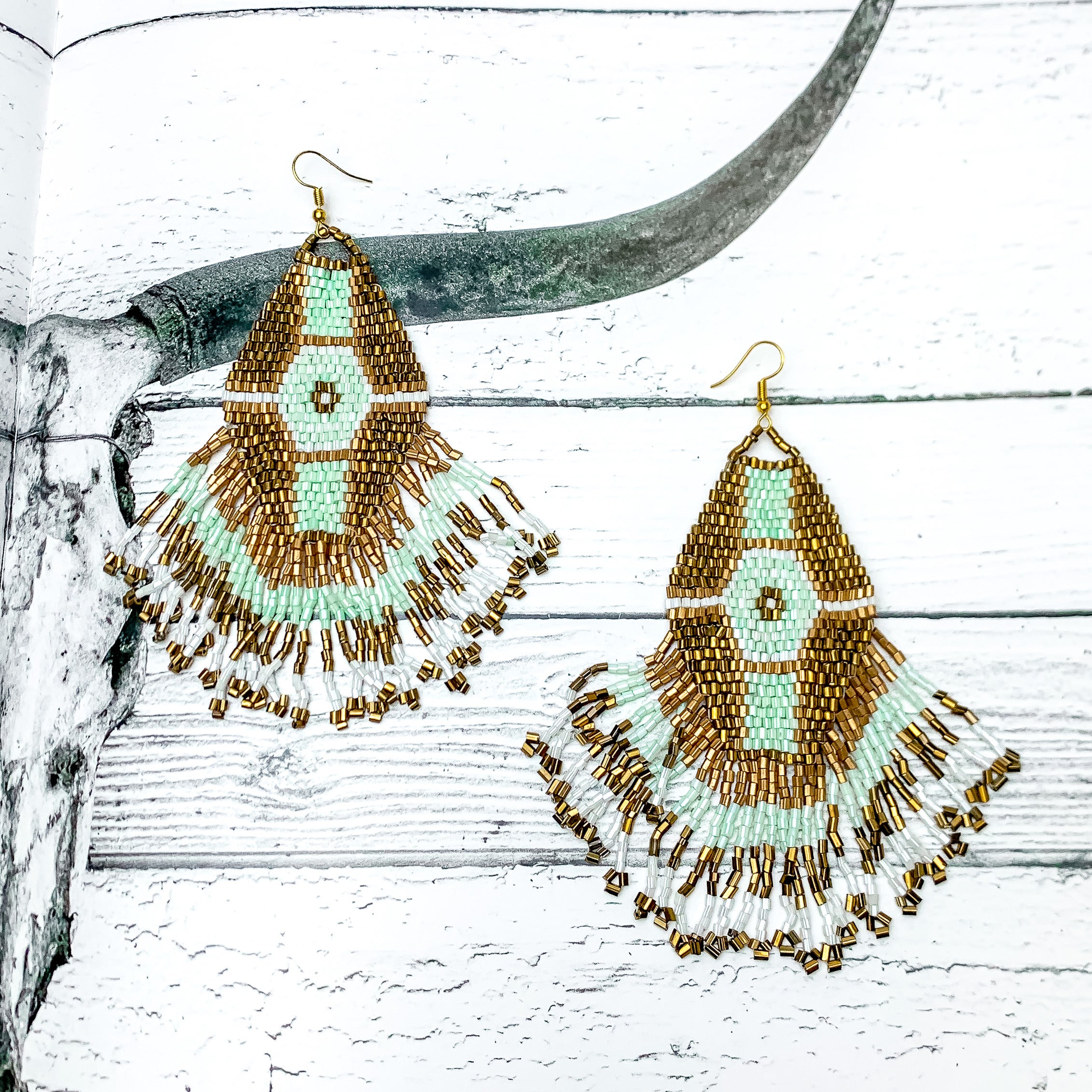Here For The Beads Dangle Earrings With Gold, White, and Blue Beads. Pictured on a wood background with a longhorn on the page.