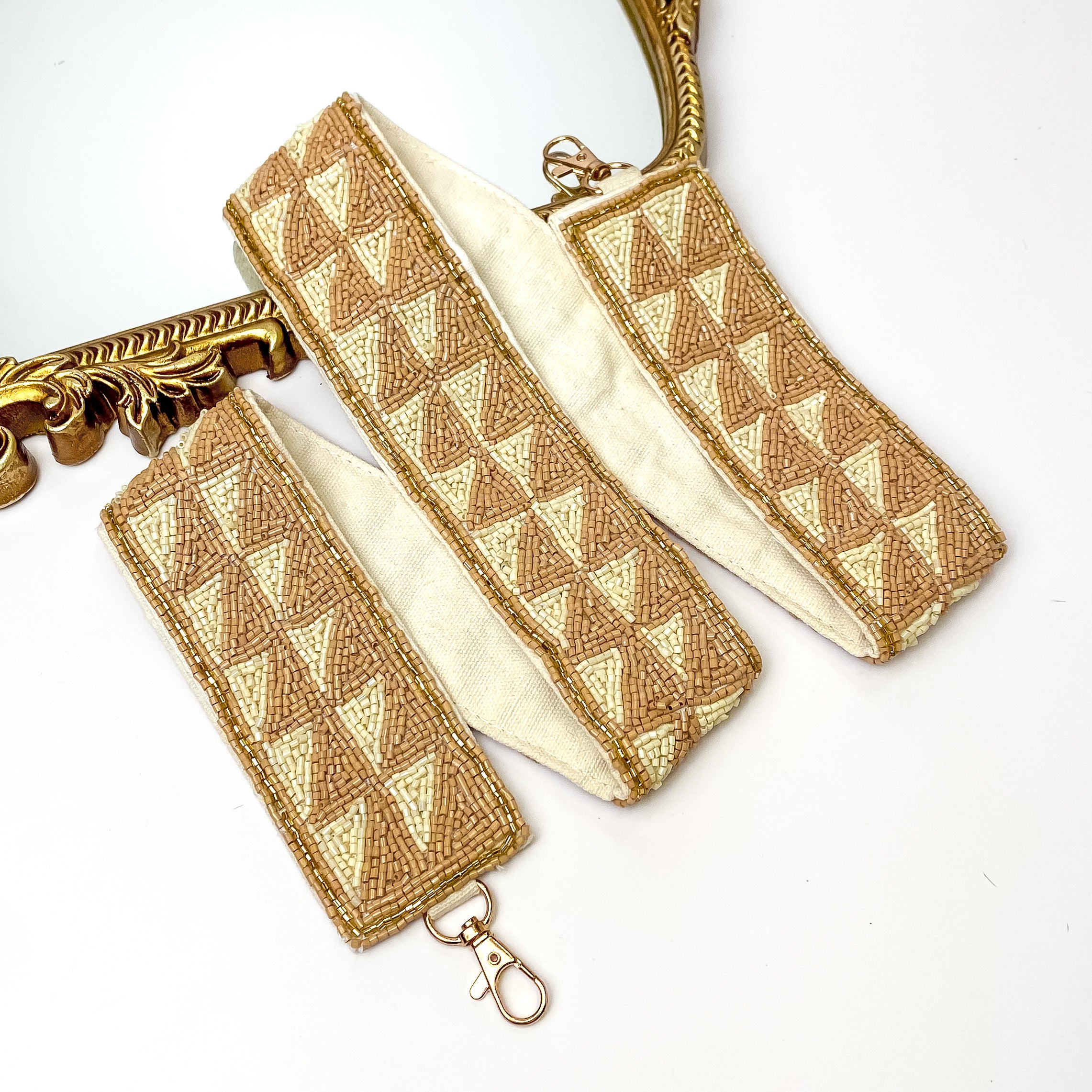 Beige and ivory beaded purse strap with gold hardware and triangle design. This purse strap is pictured partially laying on a gold mirror on a white background. 
