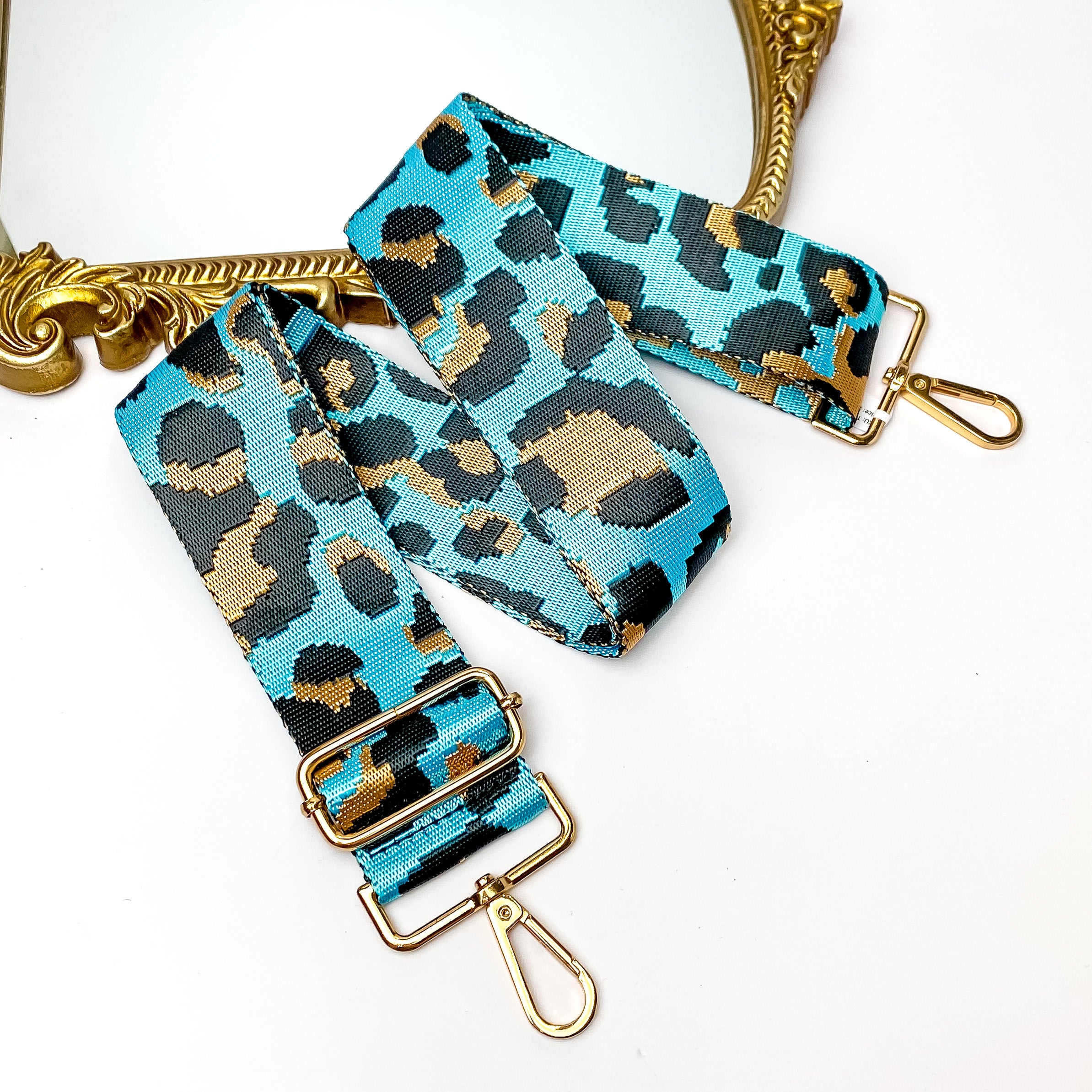 Shiny blue purse strap with a tan and black leopard print. This purse strap includes gold accents. This purse strap is pictured partially on a gold mirror on a white background.