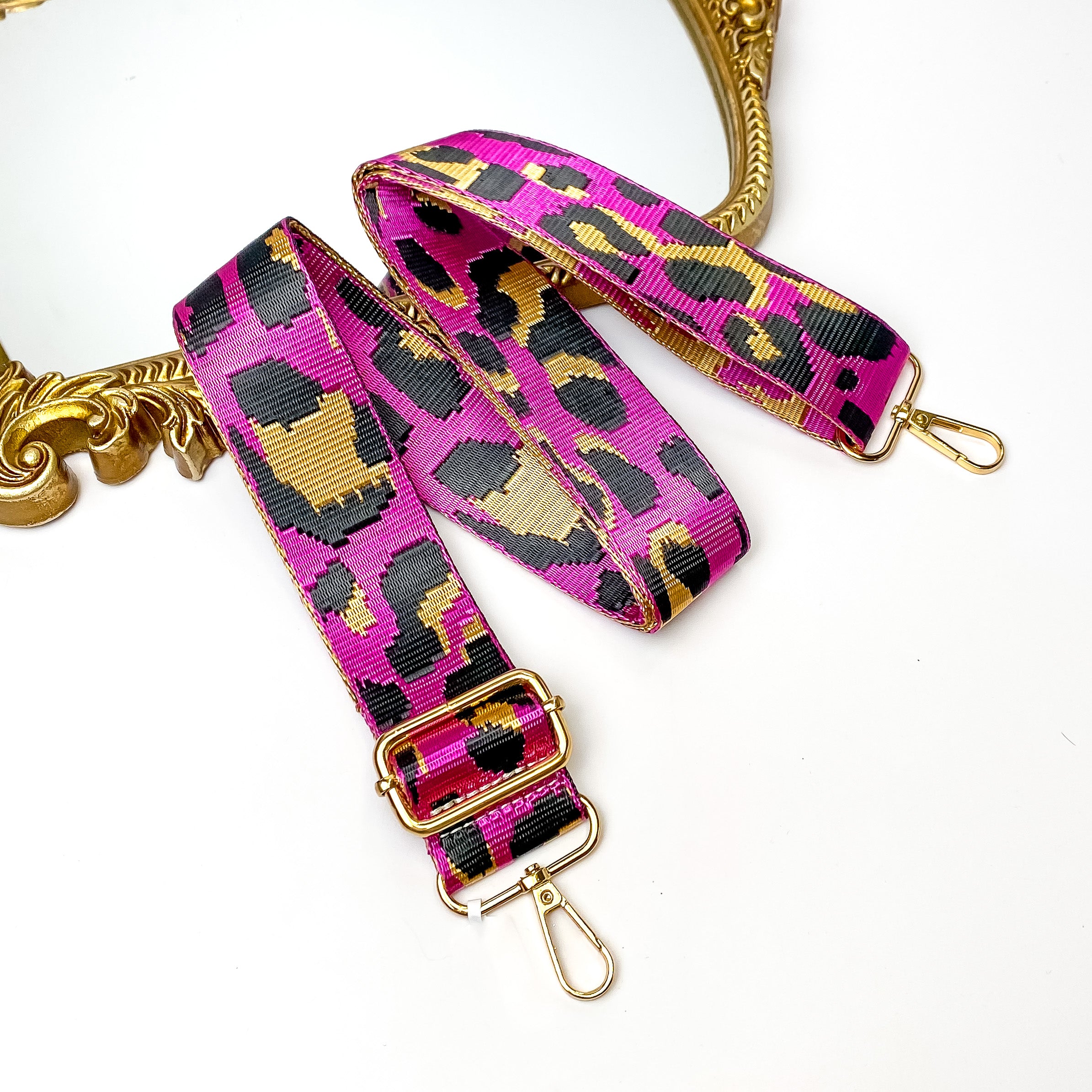 Shiny fuchsia pink purse strap with a tan and black leopard print. This purse strap includes gold accents. This purse strap is pictured partially on a gold mirror on a white background.