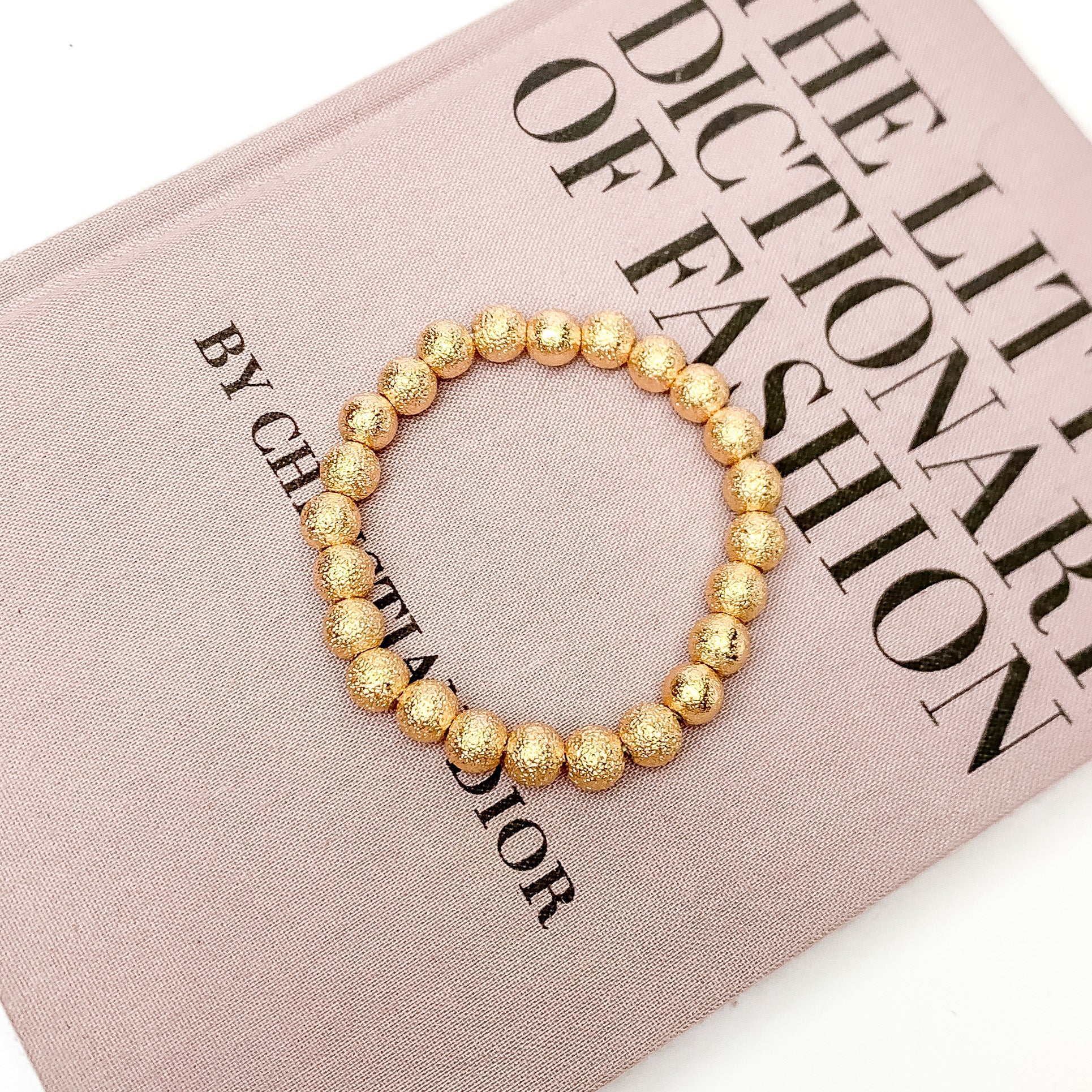 Gold Tone Basic Beaded Bracelet. Pictured laying on a book. The book is on a white background.