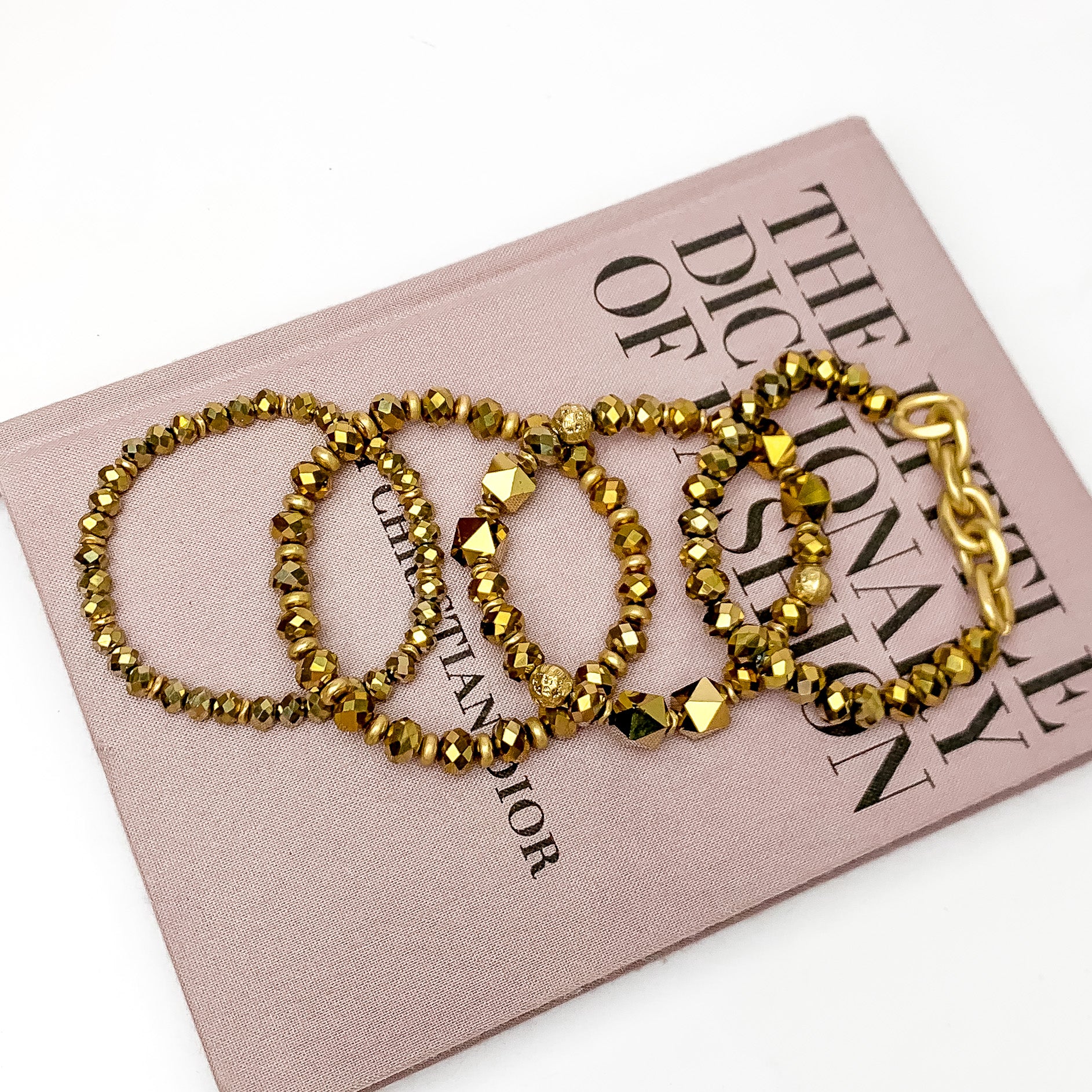 Set of Four | Glorious Gold Crystal Beaded Bracelet Set in Gold. Pictured laying on a closed book. The book is on a white background.