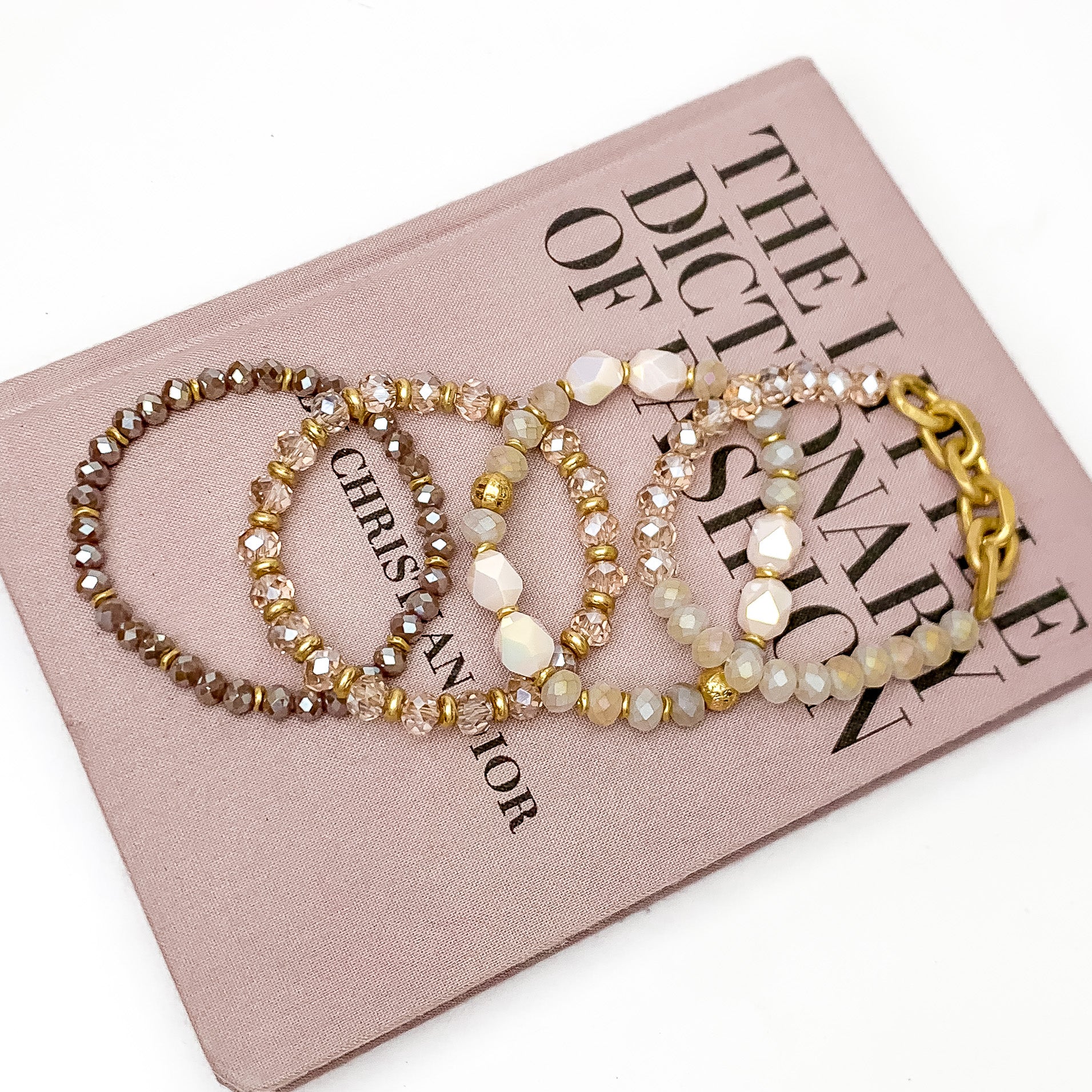 Set of Four | Glorious Gold Crystal Beaded Bracelet Set in Mauve Purple. Pictured laying on a closed book. The book is on a white background.