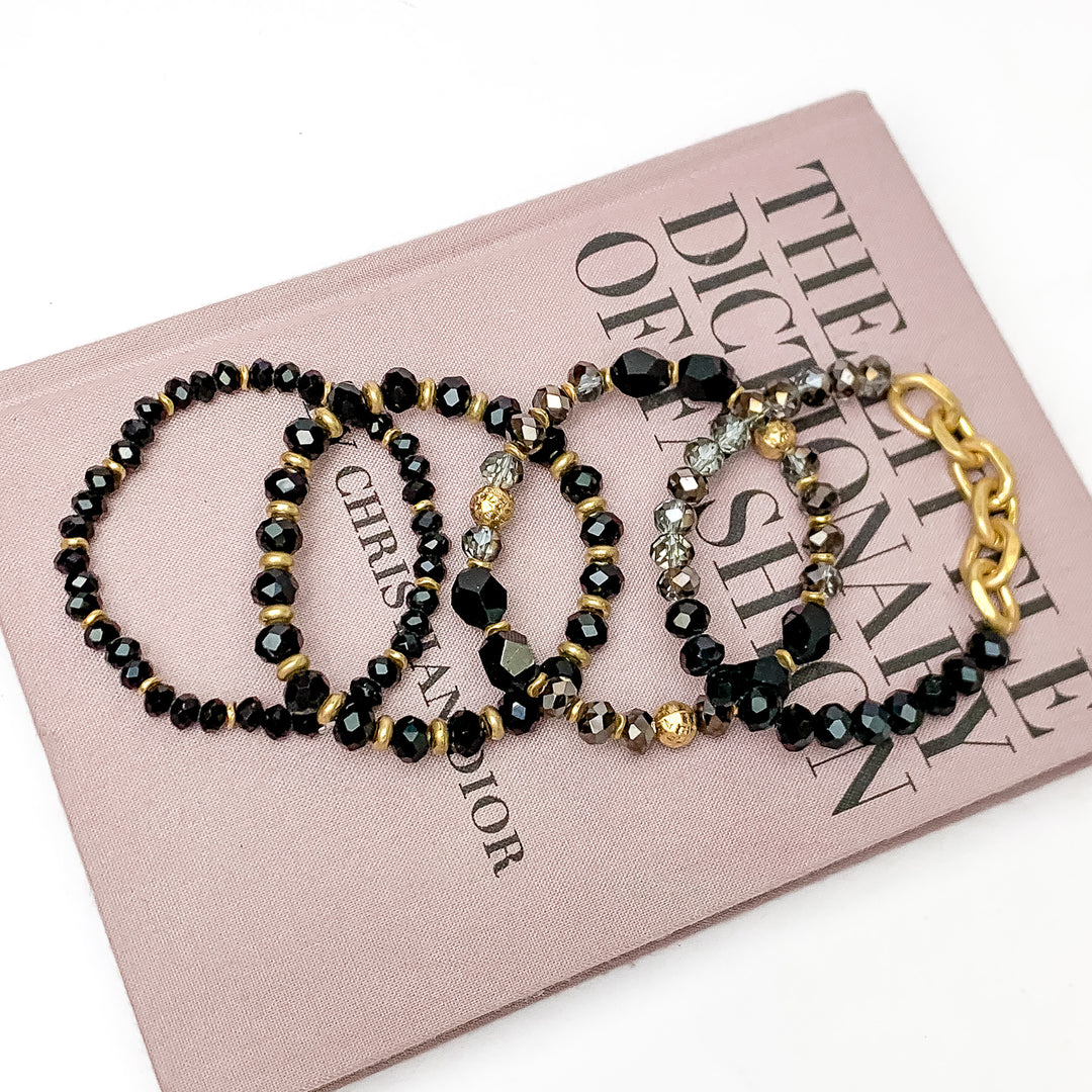 Set of Four | Glorious Gold Crystal Beaded Bracelet Set in Black. Pictured laying on a closed book. The book is on a white background.
