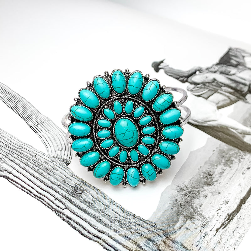 Turquoise Oval Stone Concho Hinge Cuff Bracelet. Pictured laying on top of an open book with a western picture behind the bracelet. 