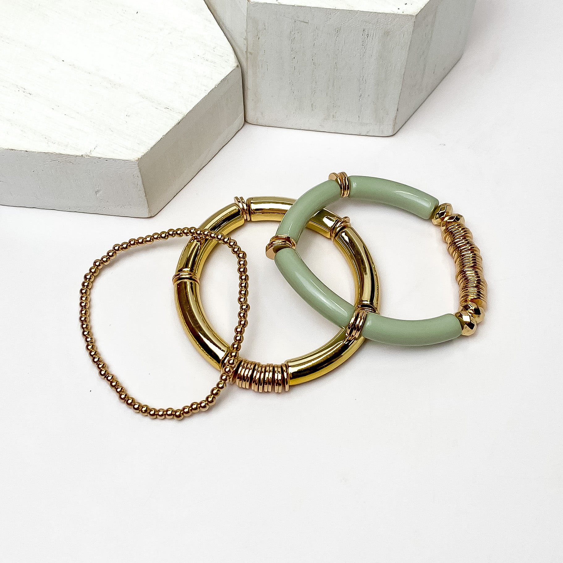 Set of Three | Bahama Nights Gold Tone Tube Bracelet Set in sage green. Pictured on a white background with white platforms above the bracelets. 