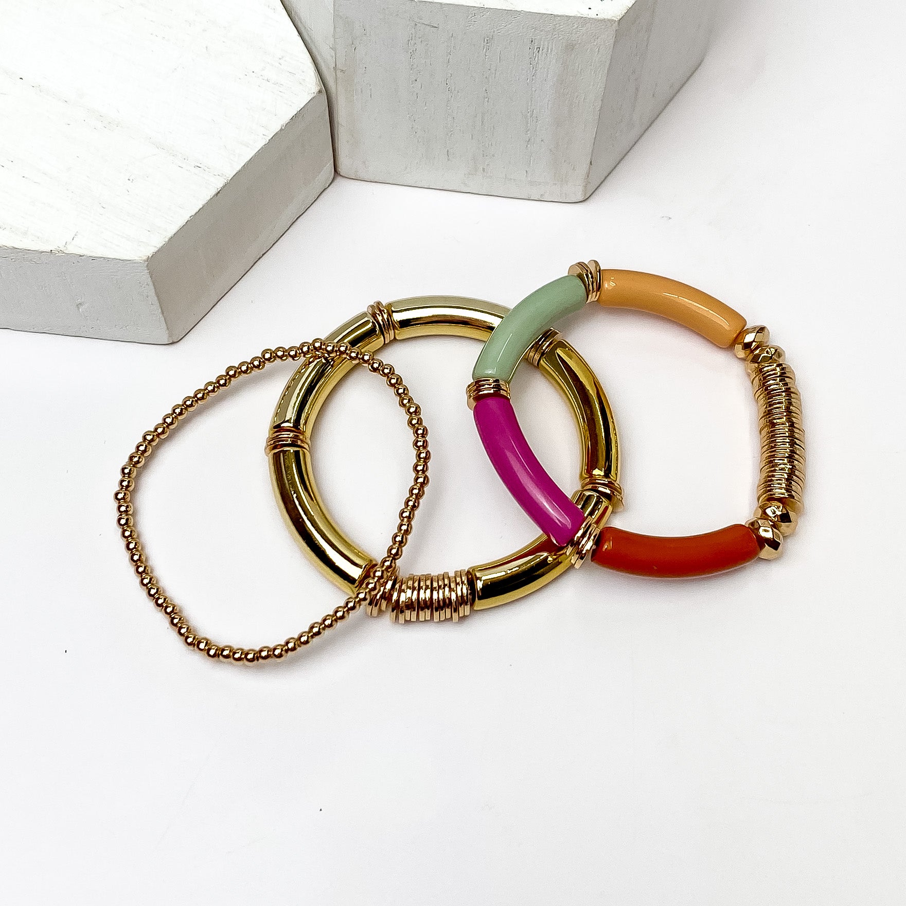 Set of Three | Bahama Nights Gold Tone Tube Bracelet Set in Multicolor. Pictured on a white background with white platforms above the bracelets. 