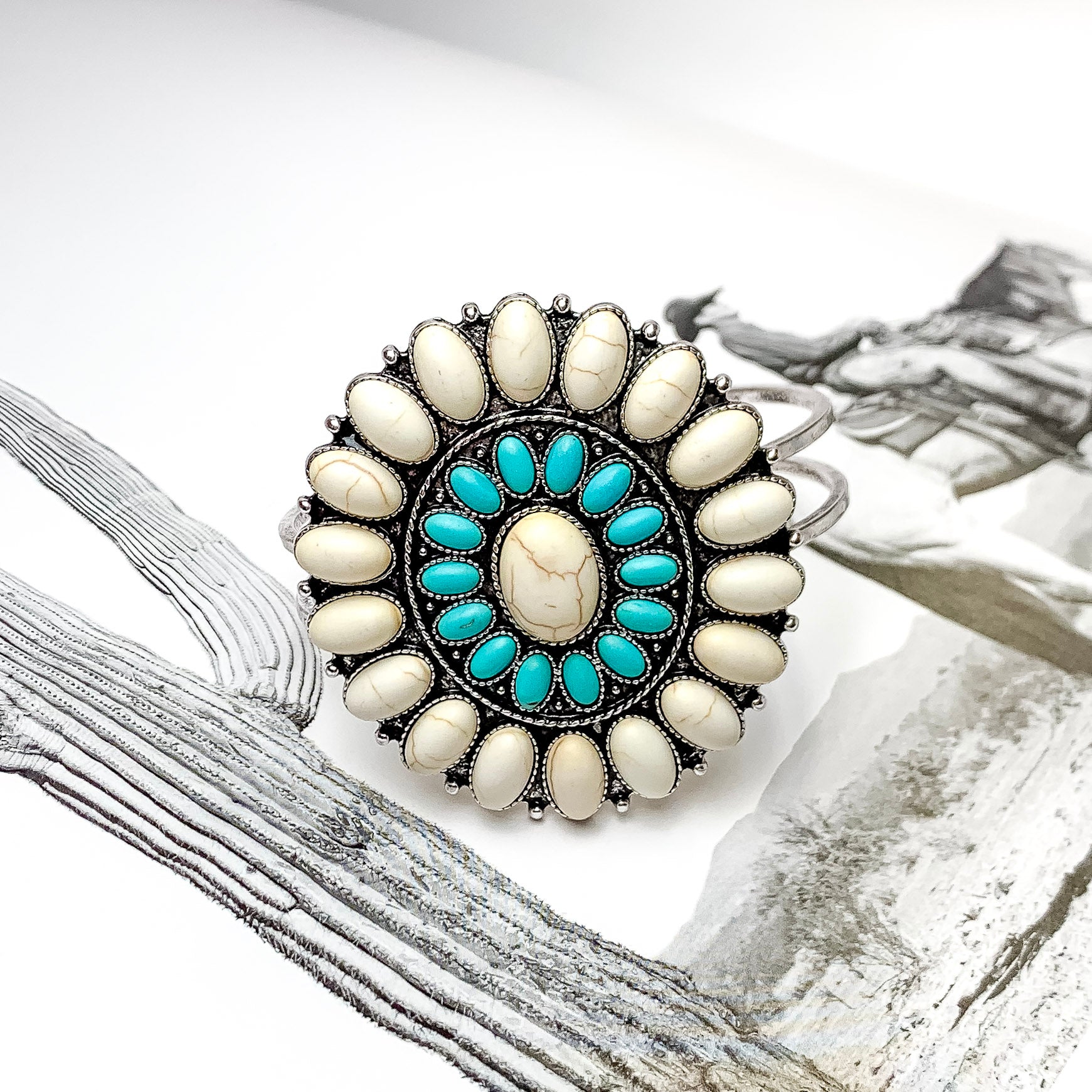 Ivory and Turquoise Oval Stone Concho Hinge Cuff Bracelet. Pictured laying on top of an open book with a western picture behind the bracelet. 
