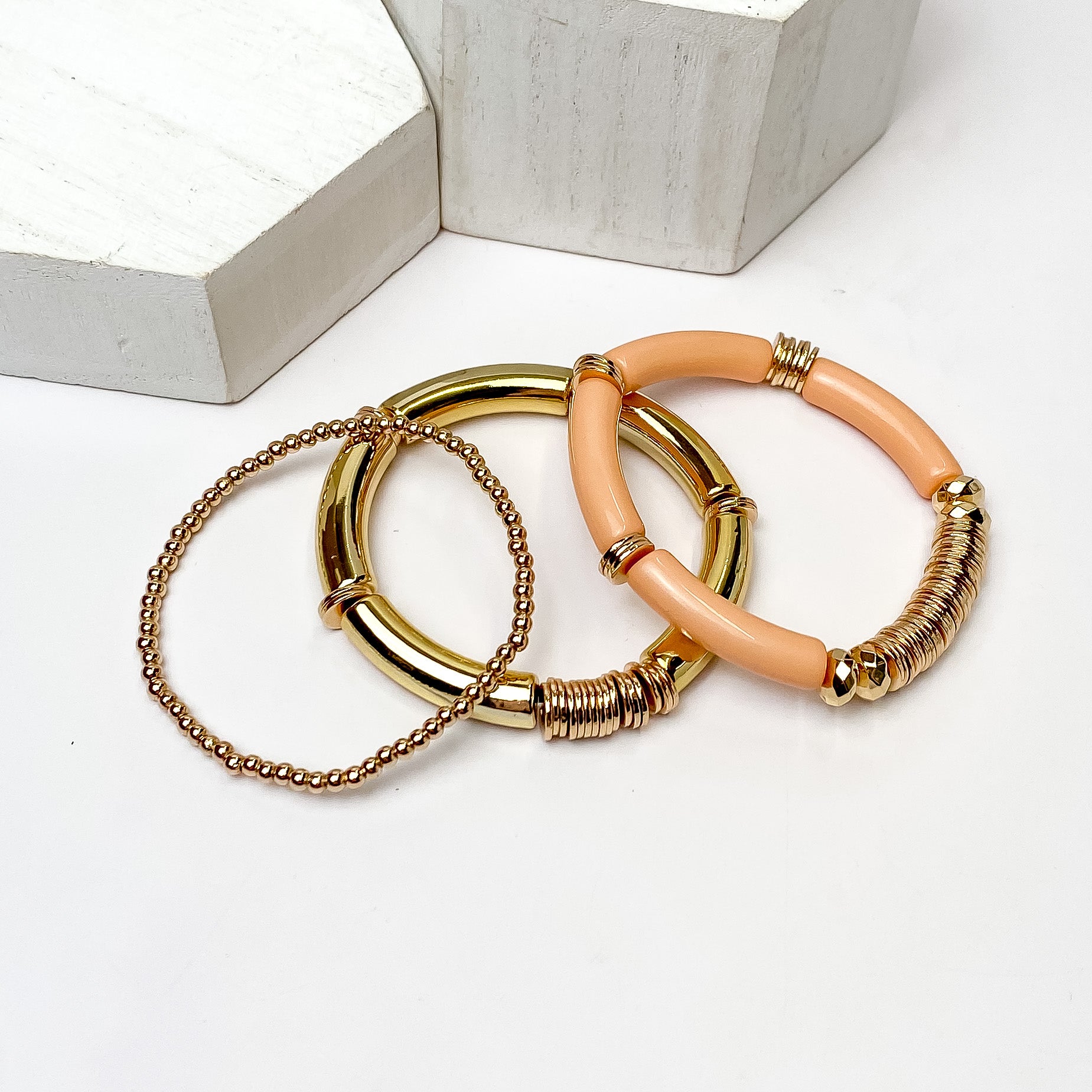 Set of Three | Bahama Nights Gold Tone Tube Bracelet Set in dusty pink. Pictured on a white background with white platforms above the bracelets.
