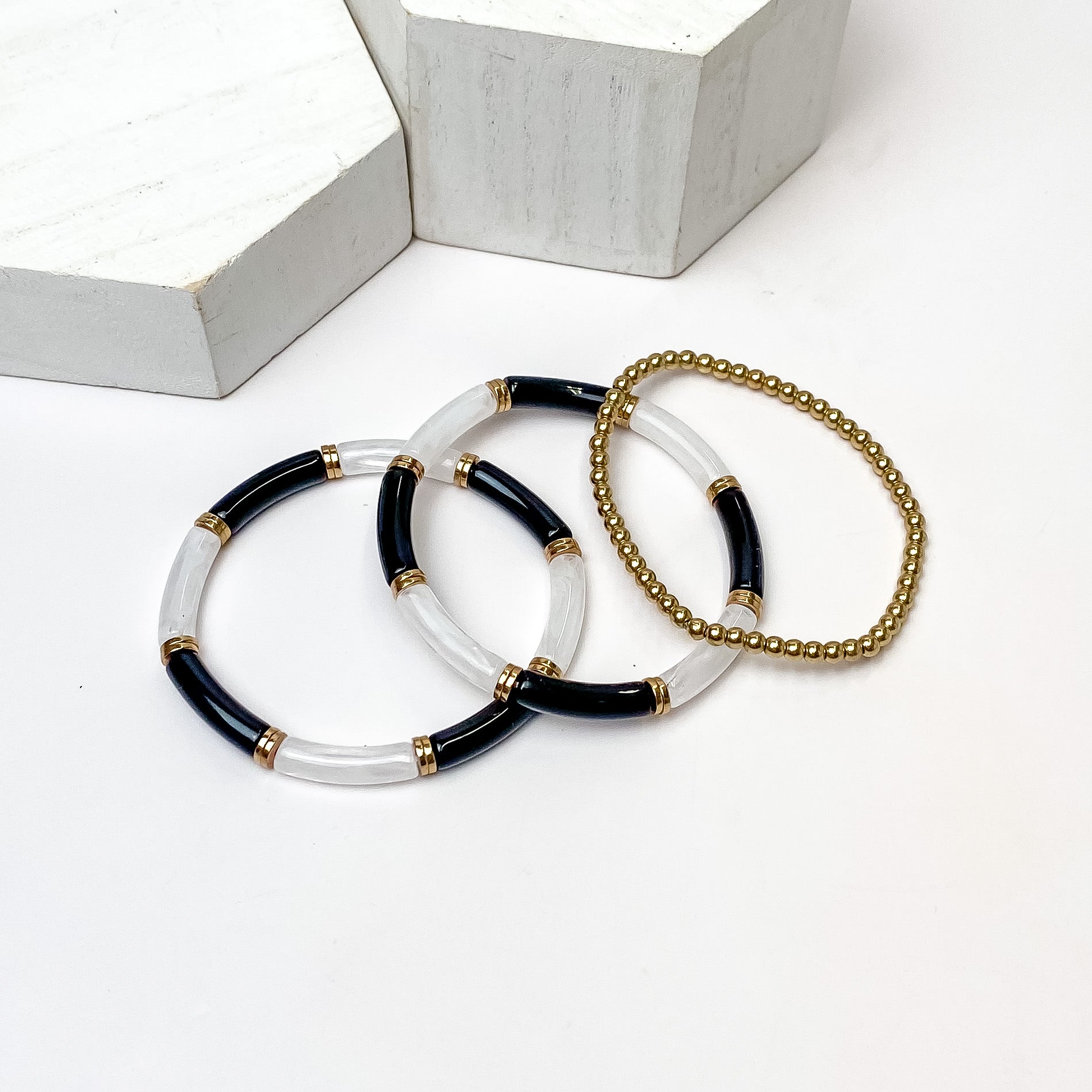Set of Three | Summer Nights Black, White, and Gold Tone Tube Bracelet Set. Pictured on a white background with white objects above the bracelets. 