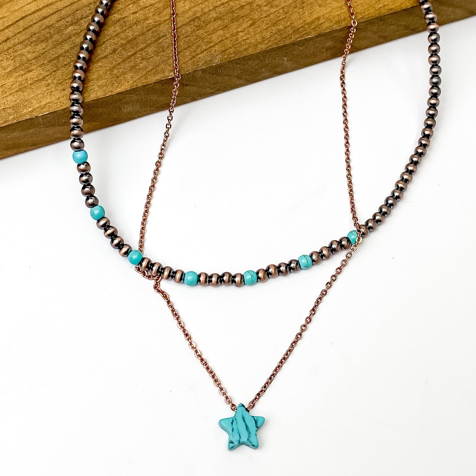 Double Layered Turquoise and Copper Faux Navajo Necklace with Star Charm. Pictured on a white and brown background. 