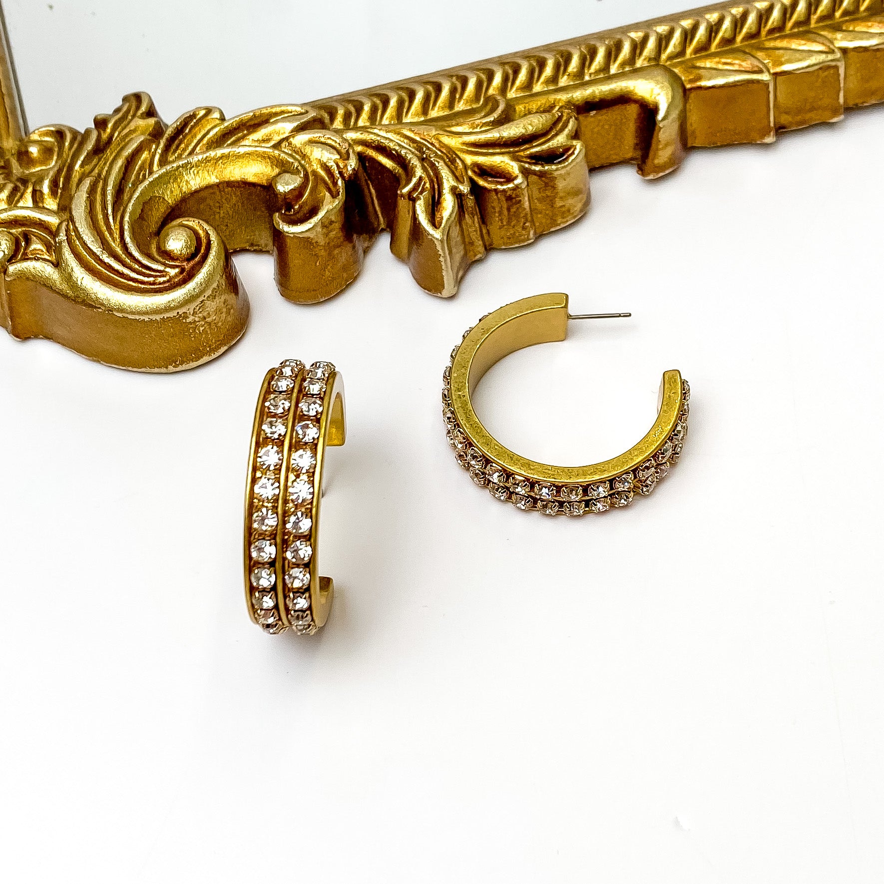 City Nights Gold Tone Hoop Earrings With Double Inlaid Clear Crystals. Pictured on a white background with a gold frame above the earrings.