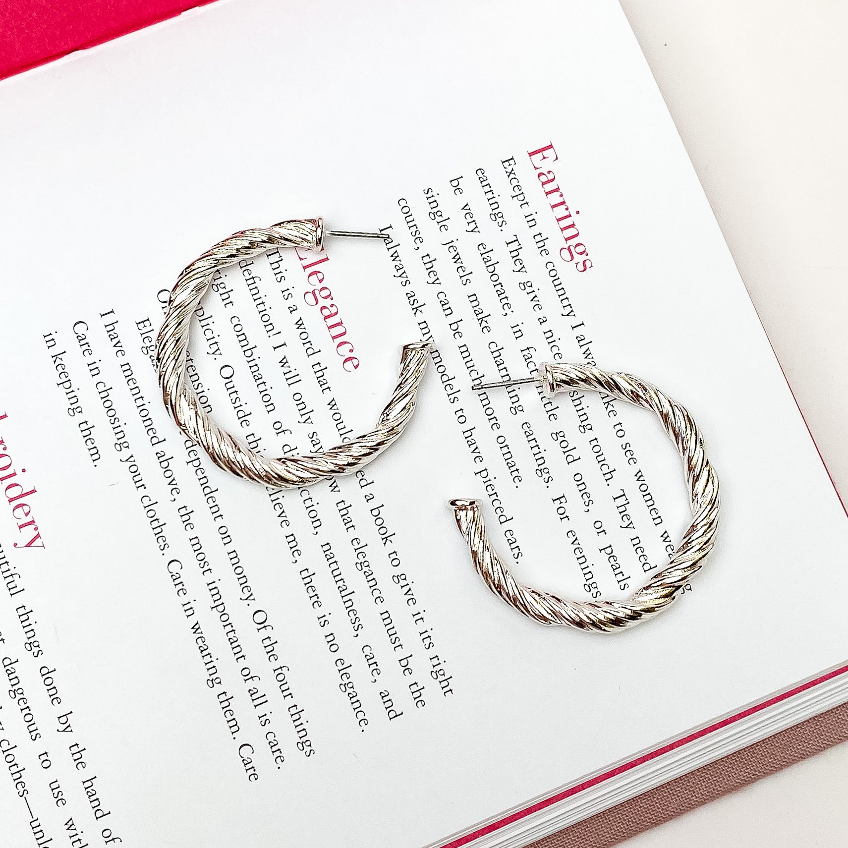 Silver twisted hoop earrings. These earrings are pictured on a open book on a white background. 