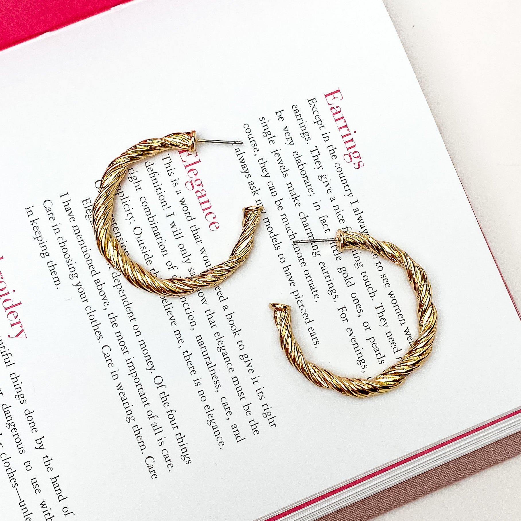 Gold twisted hoop earrings. These earrings are pictured on a open book on a white background. 