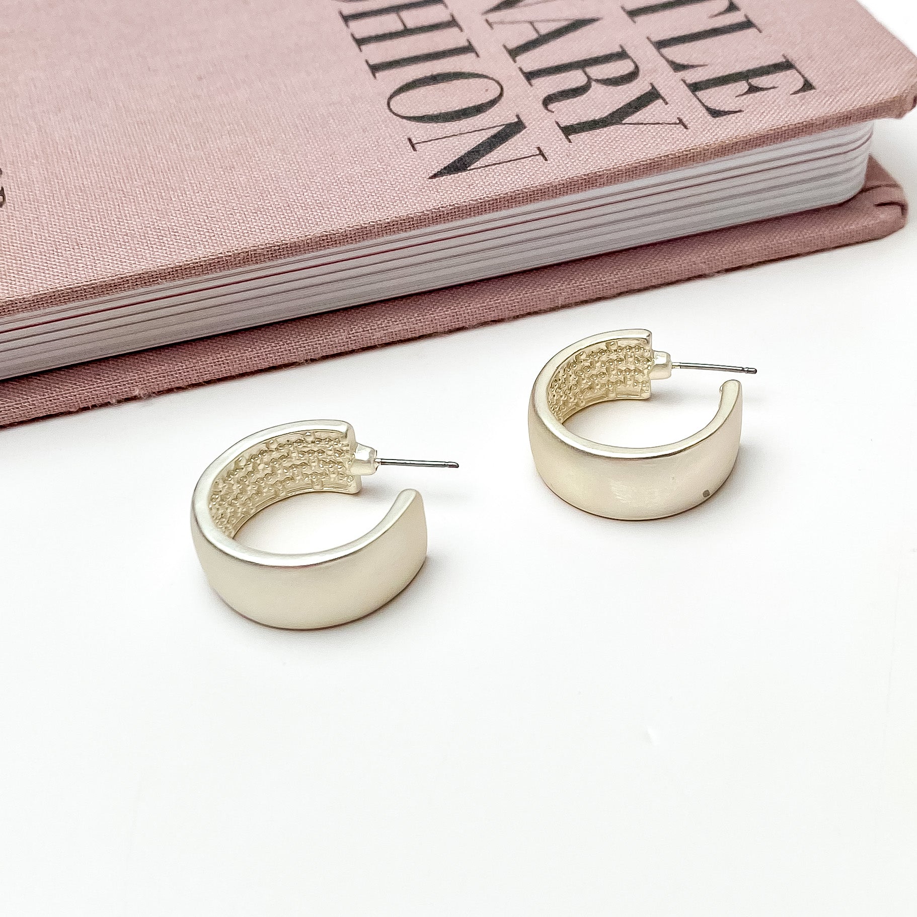 Silver Tone Hoop Earrings With a Textured Inside. Pictured on a white background with a book laying above the earrings.