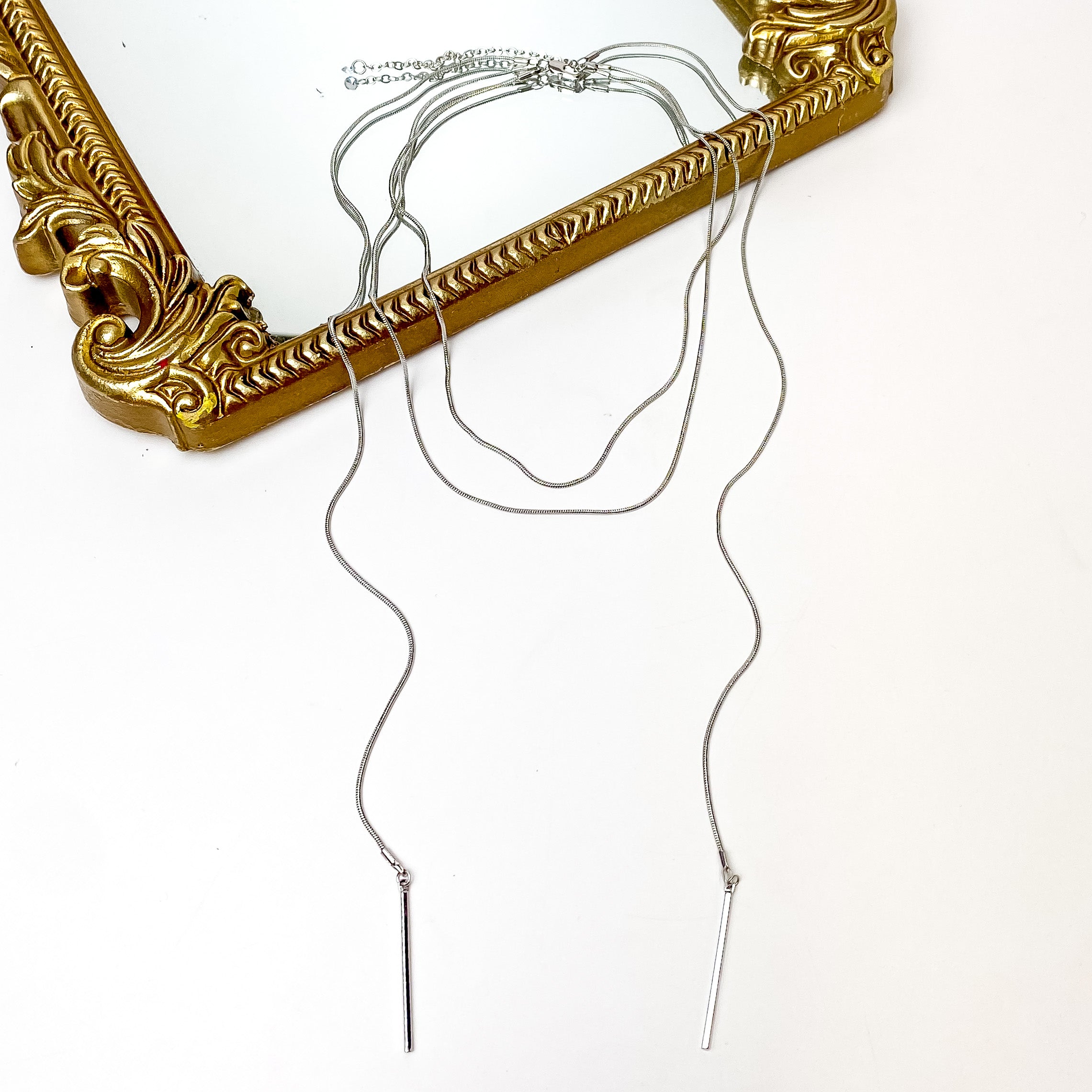 Wrap Around Necklace With Metal Accessory in Silver Tone. Pictured on a white background with part of the necklace laying on a mirror with a gold trim.