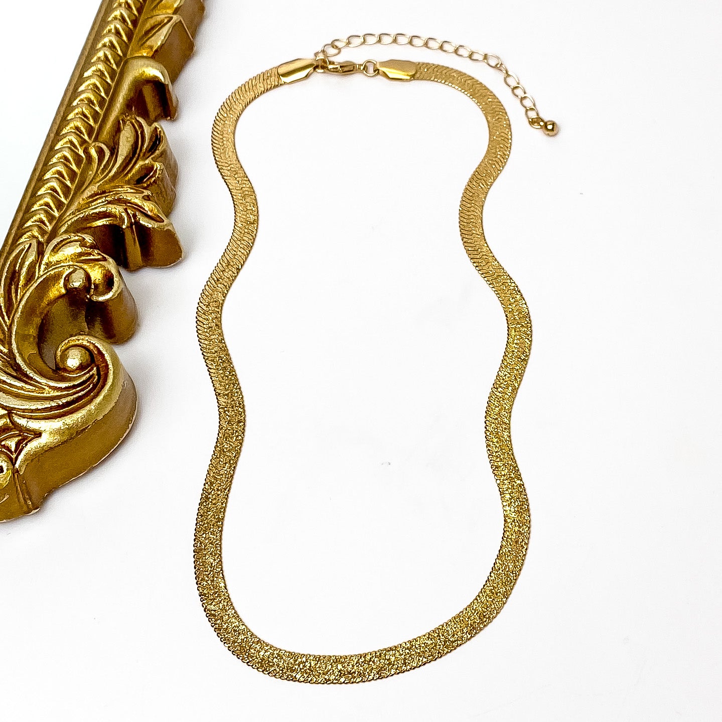 Gold herringbone chain necklace with a gold necklace adjuster. This necklace is pictured on a white background with a gold mirror on the left side. 
