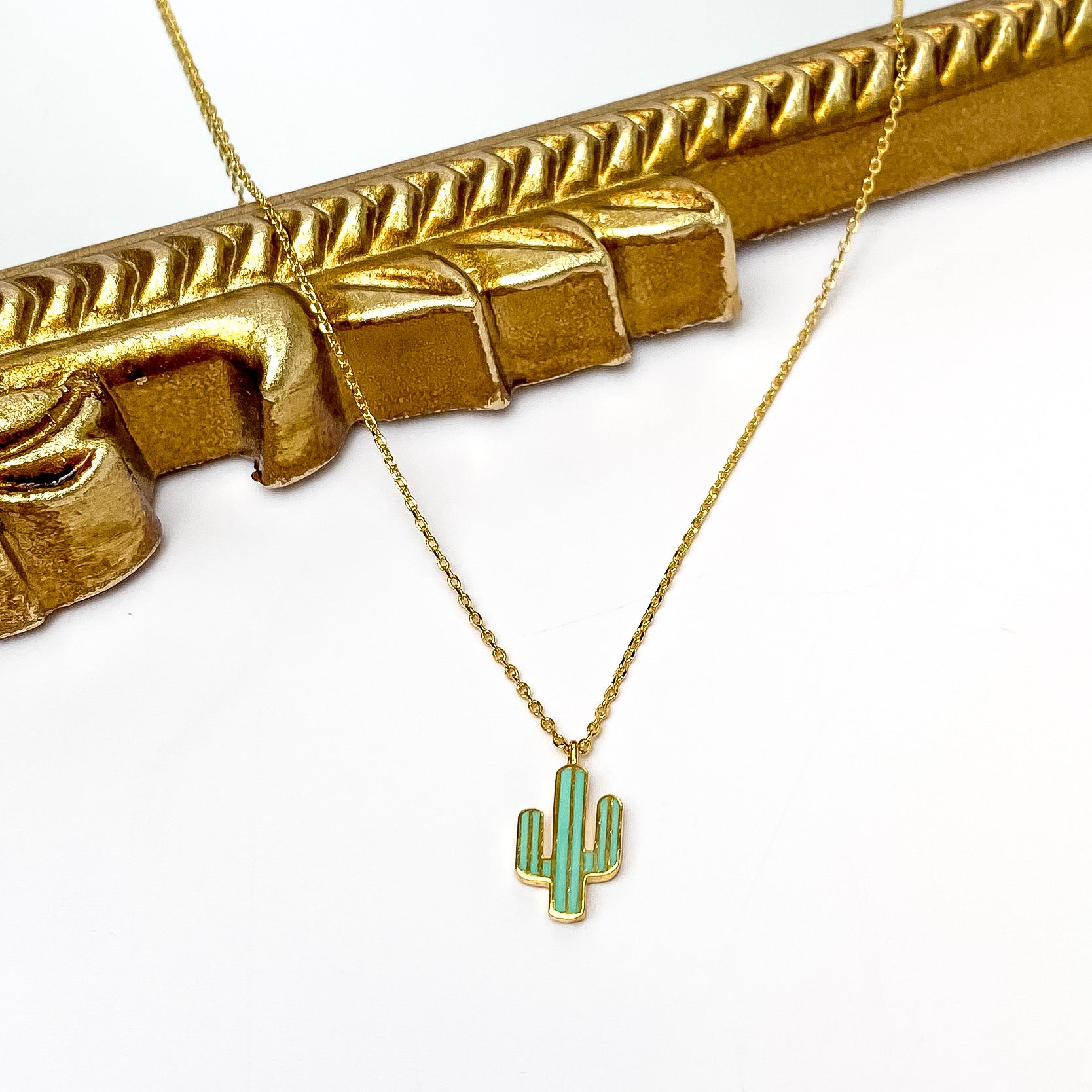 Gold Tone Necklace With Green Cactus Charm. Pictured on a white background with part of the necklace laying on a mirror with gold trim.