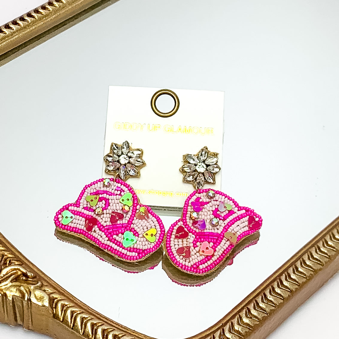 White and hot pink beaded cowboy hat earrings. Crystal flower posts. Pictured on a mirror with a gold trim. 