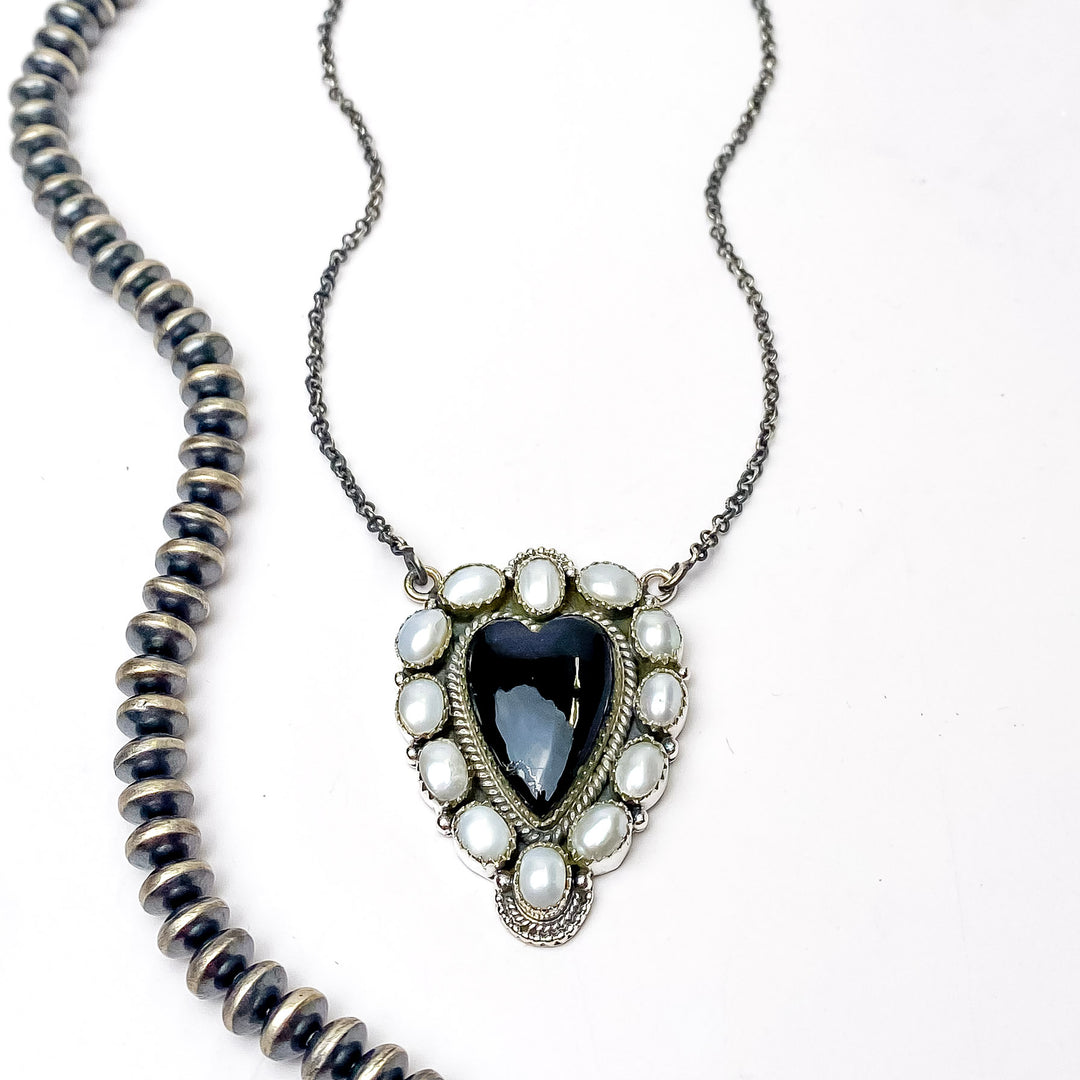 In the picture is a handmade sterling silver with white pearl outline cluster design with a black heart pendant center with a white background