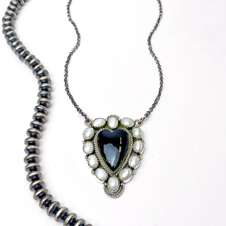 In the picture is a handmade sterling silver with white pearl outline cluster design with a black heart pendant center with a white background