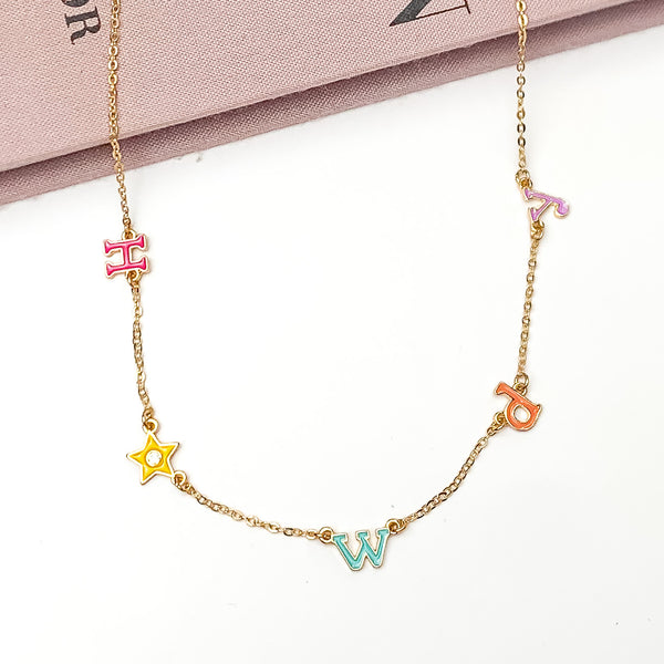 Howdy Gold Tone Chain Necklace in Multicolor. Pictured on a white background with the top of the necklace laying on a book. 
