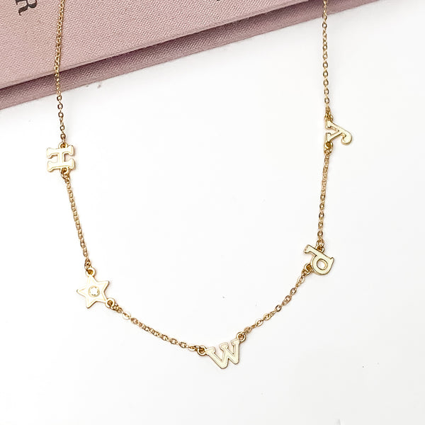 Howdy Gold Tone Chain Necklace in White. Pictured on a white background with the top of the necklace laying on a book.