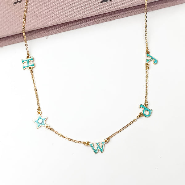 Howdy Gold Tone Chain Necklace in Turquoise Blue. Pictured on a white background with the top of the necklace laying against a book.