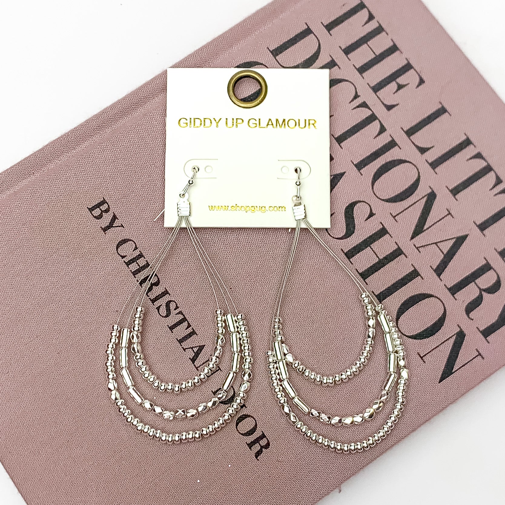 Layered Open Teardrop Earrings With Beads in Silver Tone. Pictured on a white background with the earrings laying on a pink book.