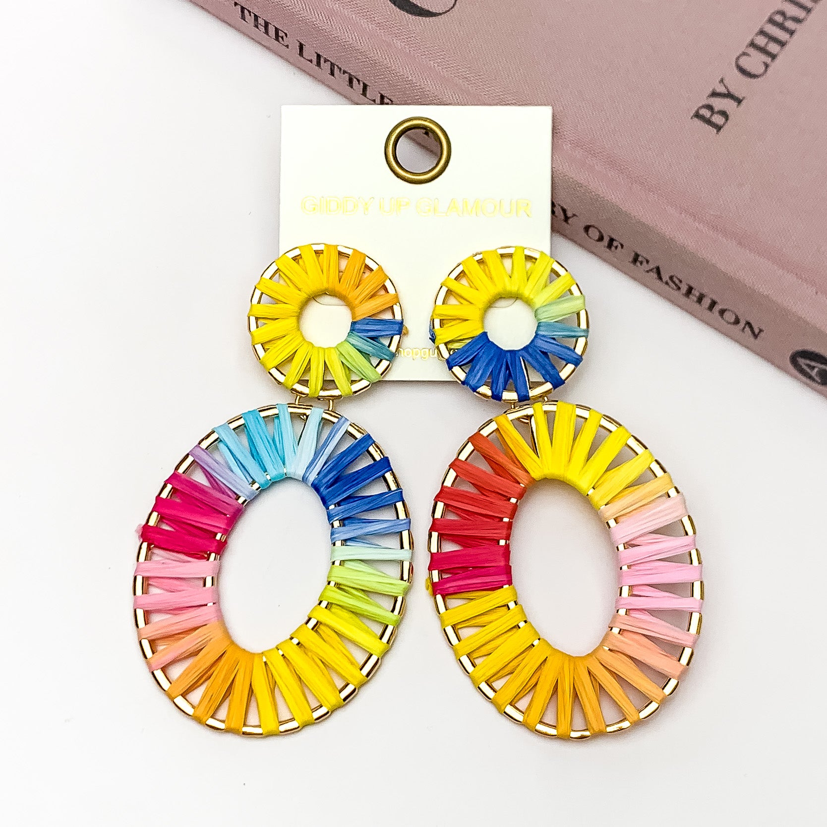 Rainbow Sunshine Open Oval Earrings in Multicolor. Pictured on a white background with the earrings laying against a pink book.
