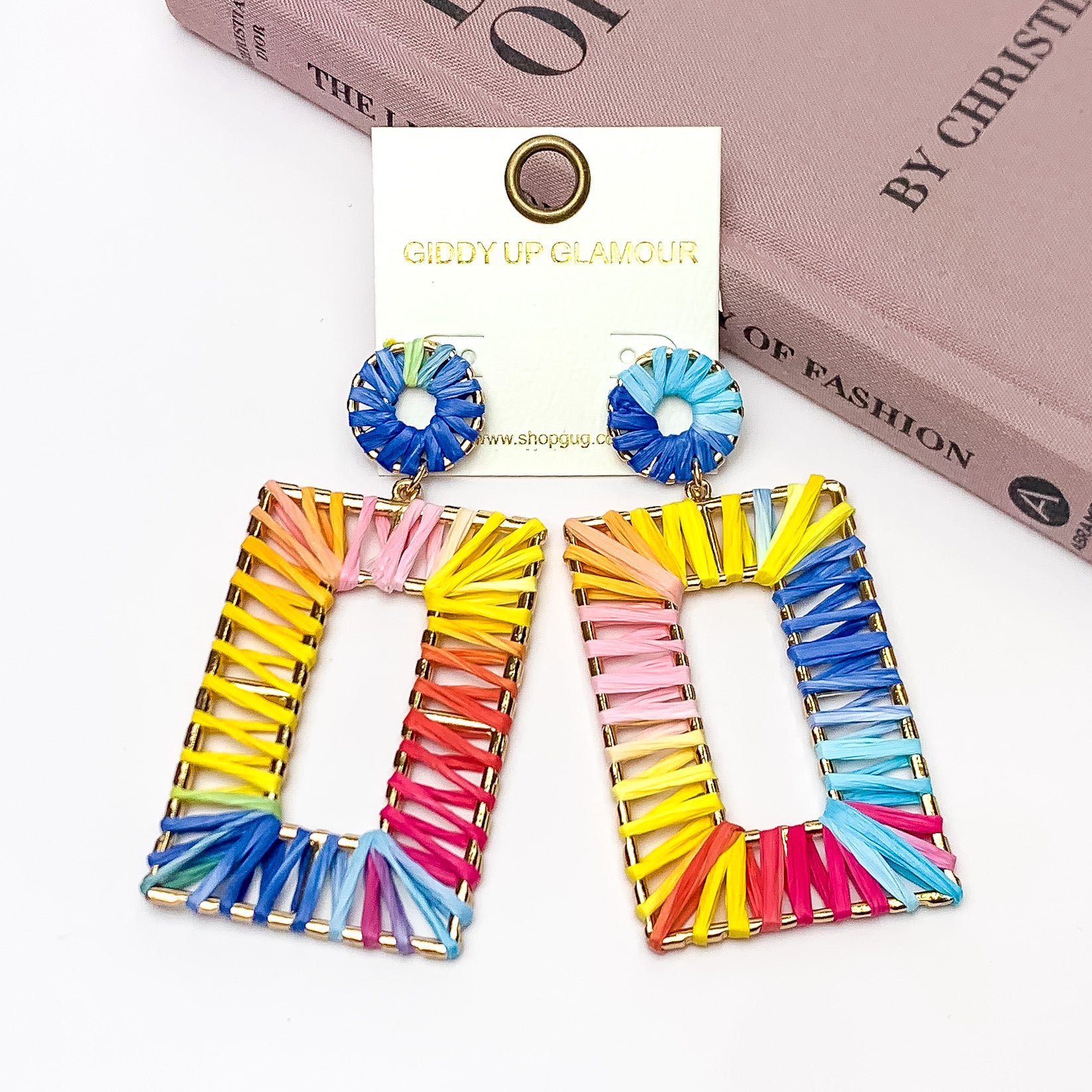 Rainbow Sunshine Open Rectangle Earrings in Multicolor. Pictured on a white background with the earrings laying against a book.