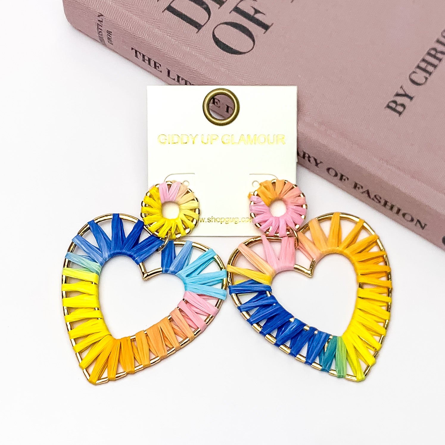 Rainbow Sunshine Open Heart Earrings in Multicolor. Pictured on a white background with the earrings laying against a pink book.