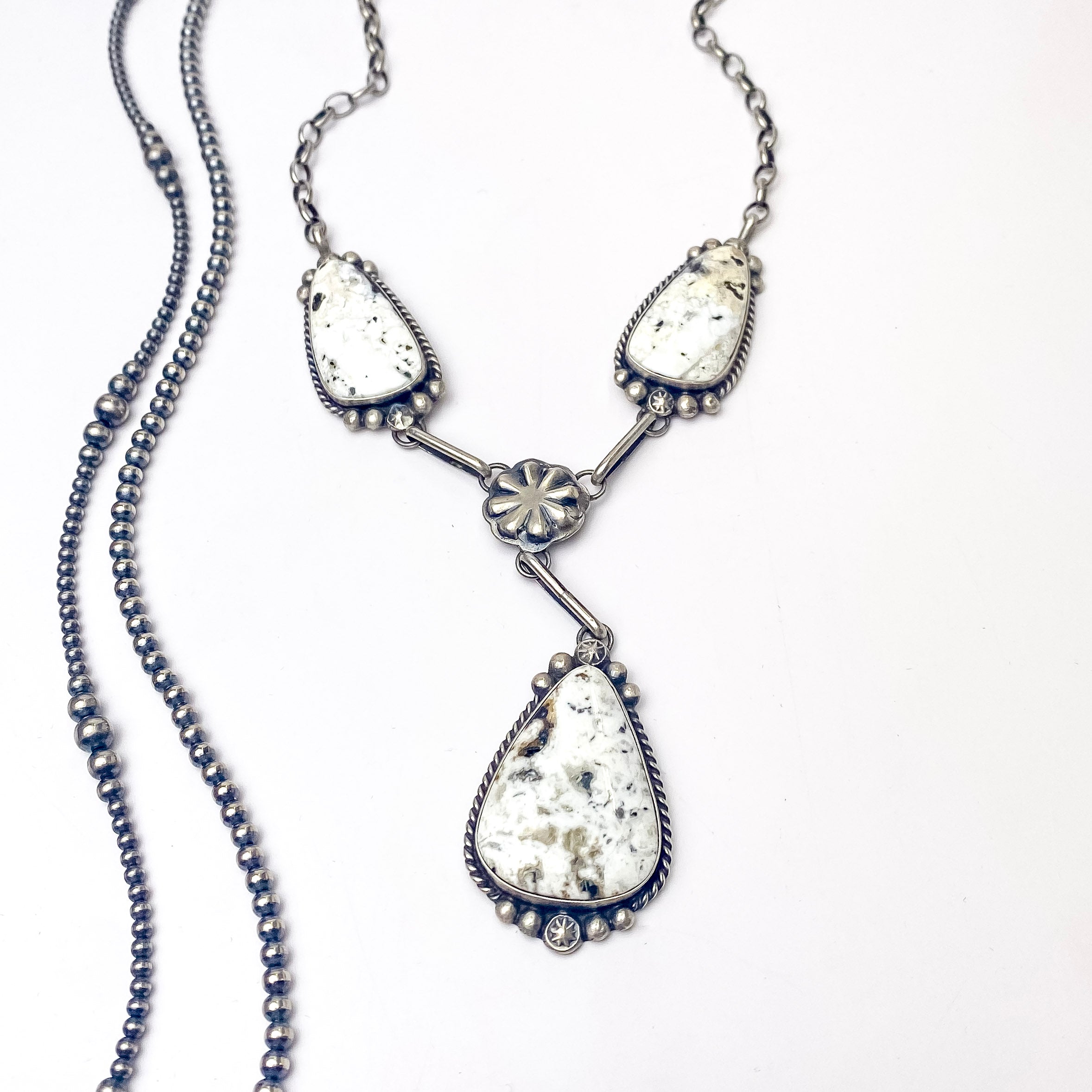In the picture is a handmade augustine largo with sterling silver and white buffalo, this stunning necklace features drop triangle pendants and a flower middle with a white background