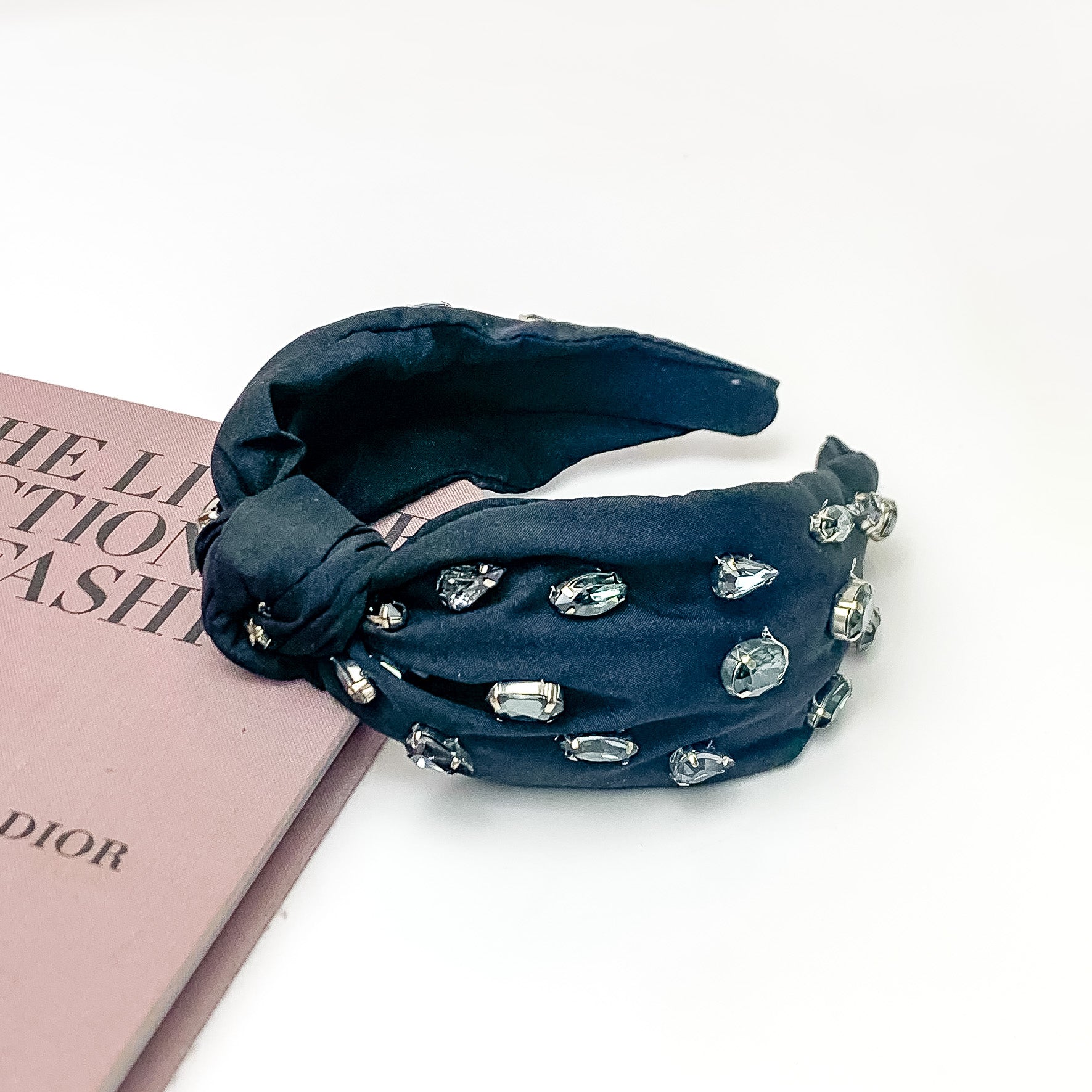 Crystal Detailed Knot Headband in Black. Pictured on a white background with the headband laying against a pink book.