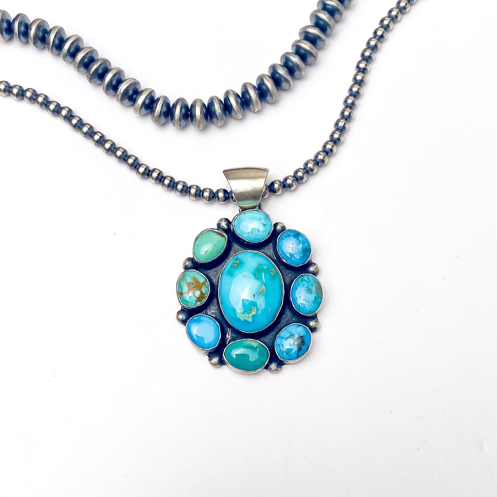In the picture is a navajo handmade sterling silver circle pendant with kingman turquoise with a white background