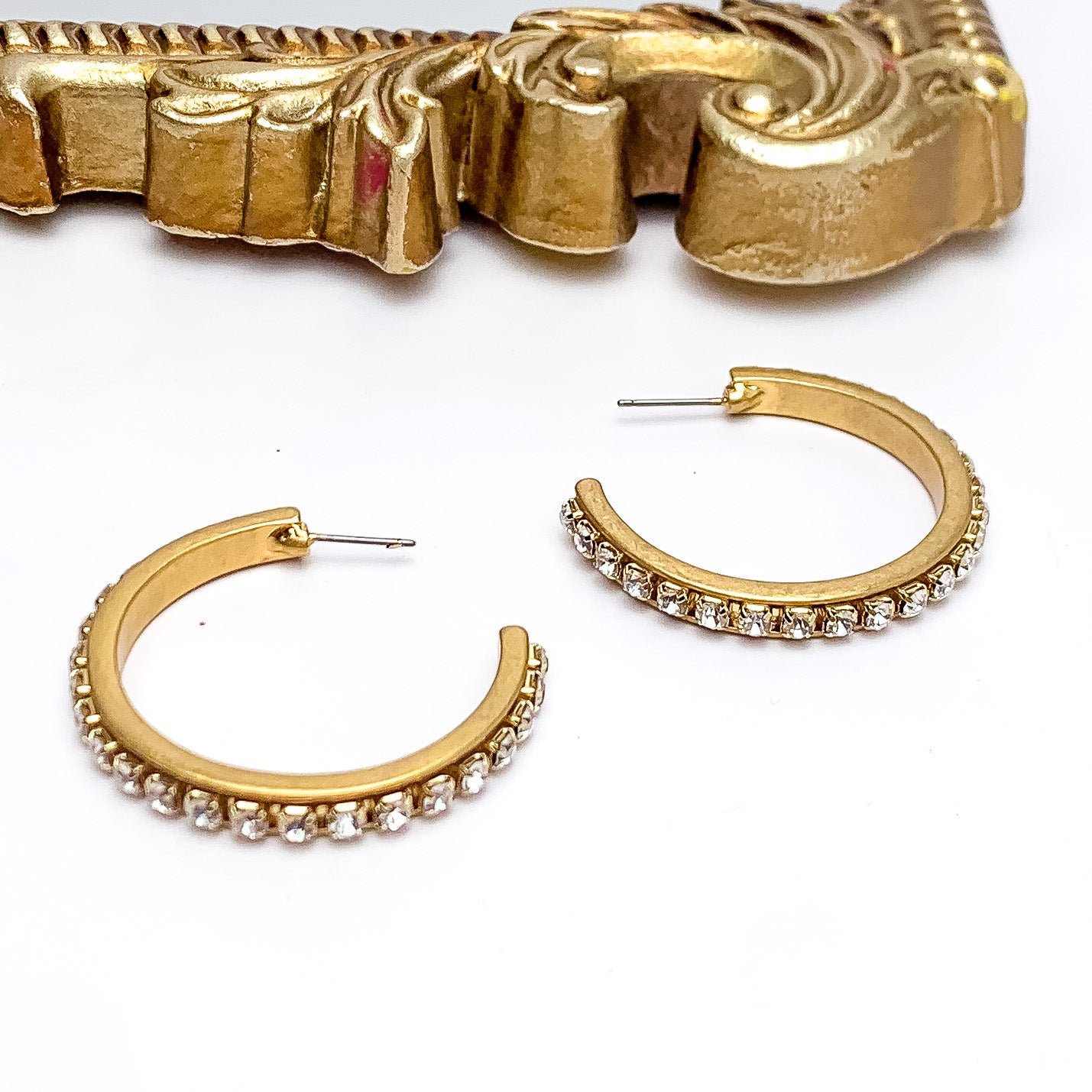 City Nights Gold Tone Hoop Earrings With Inlaid Clear Crystals. Pictured on a white background with a gold frame above the earrings.