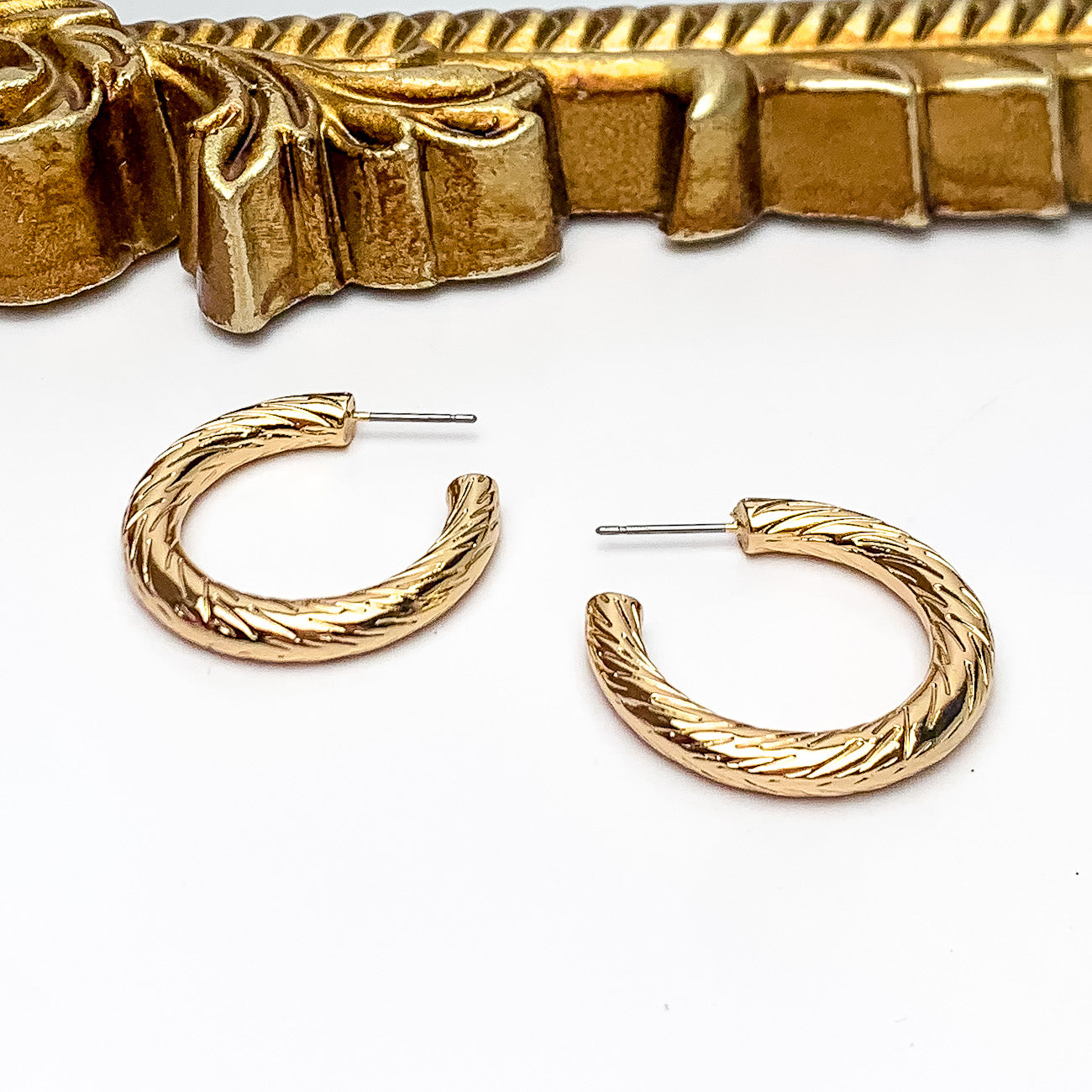 Gold Tone Small Twisted Hoop Earrings. Pictured on a white background with a gold frame above the earrings.