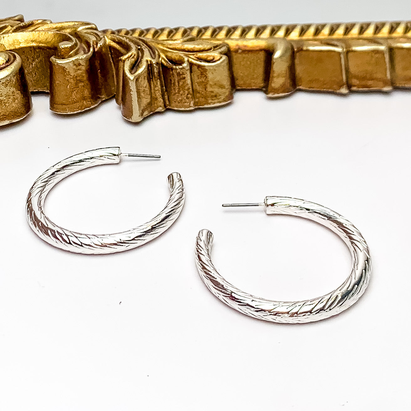 Silver Tone Large Twisted Hoop Earrings. Pictured on a white background with gold frame above the earrings.