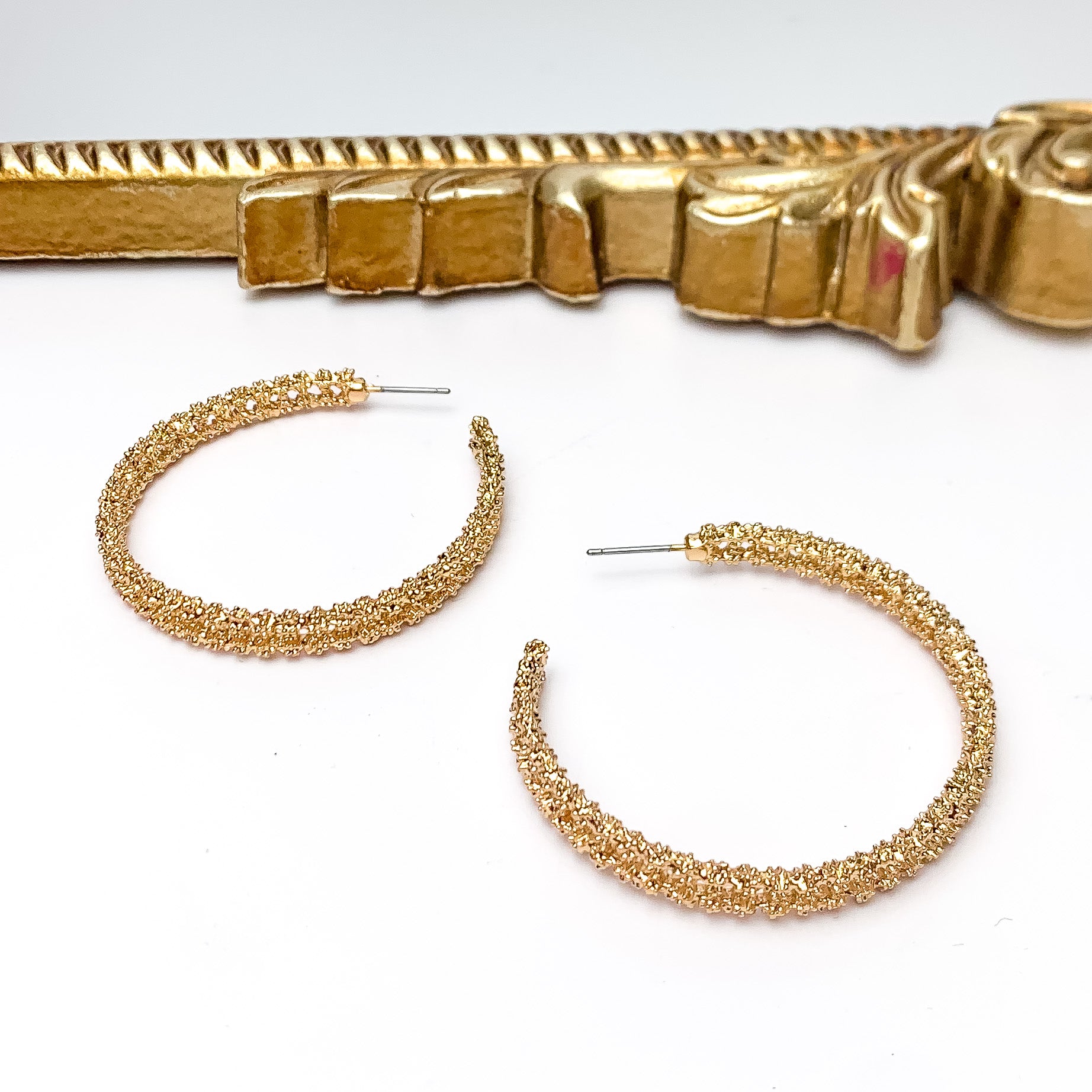 Worry Free Large Gold Tone Textured Hoop Earrings. Pictured on a white background with a gold frame above the earrings.